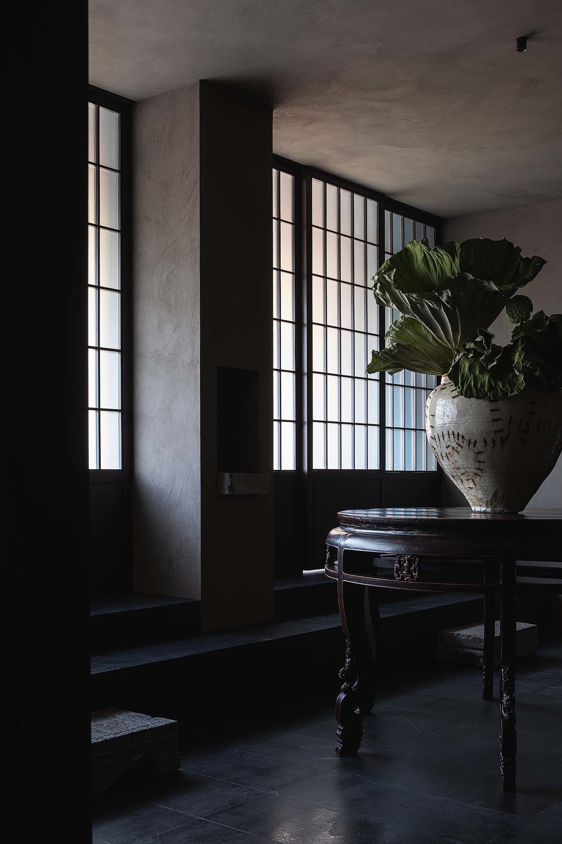 A modern industrial lobby featuring stone walls and a large vase with green plants.