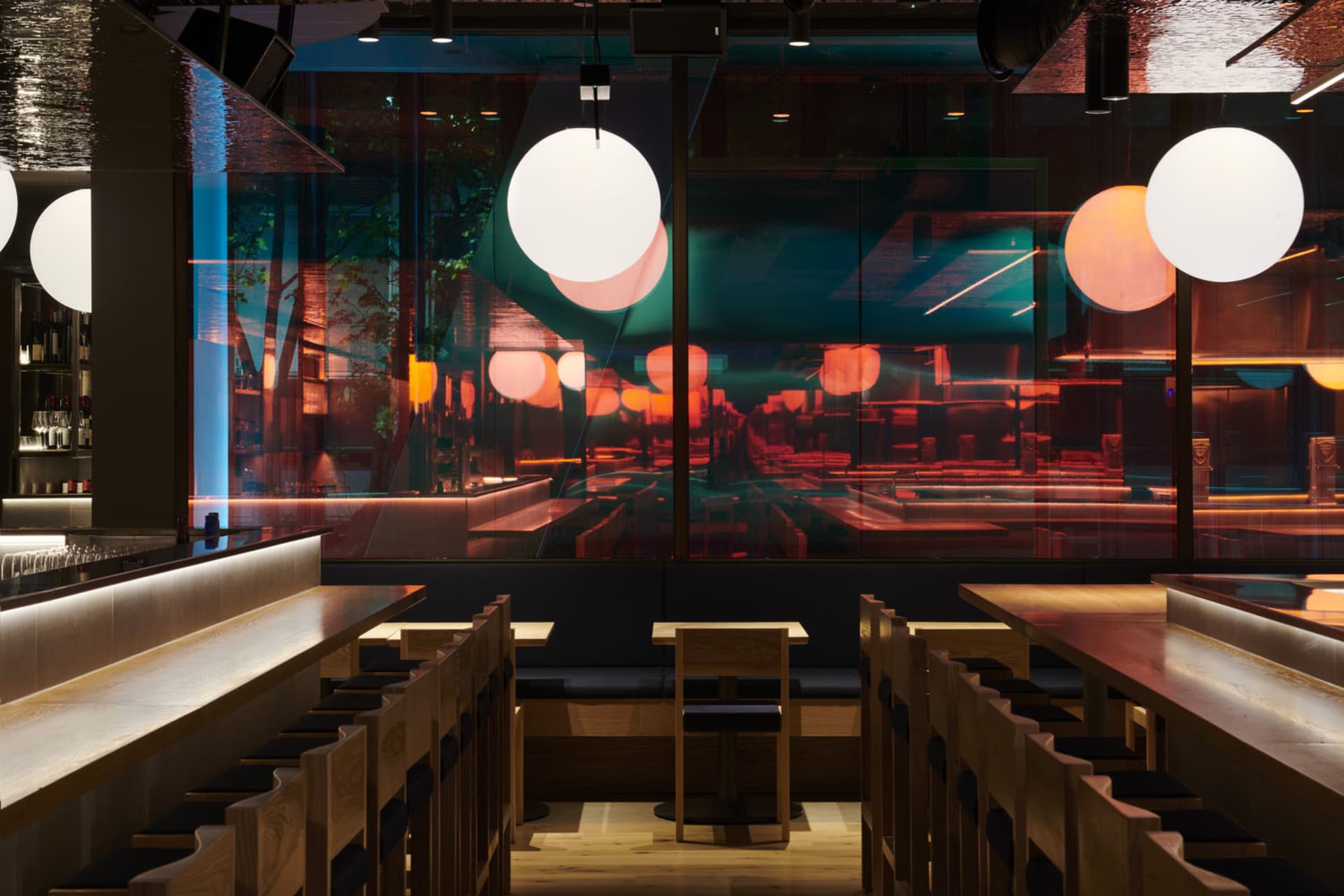 Modern restaurant interior with wooden benches, marble tables, and glass walls.