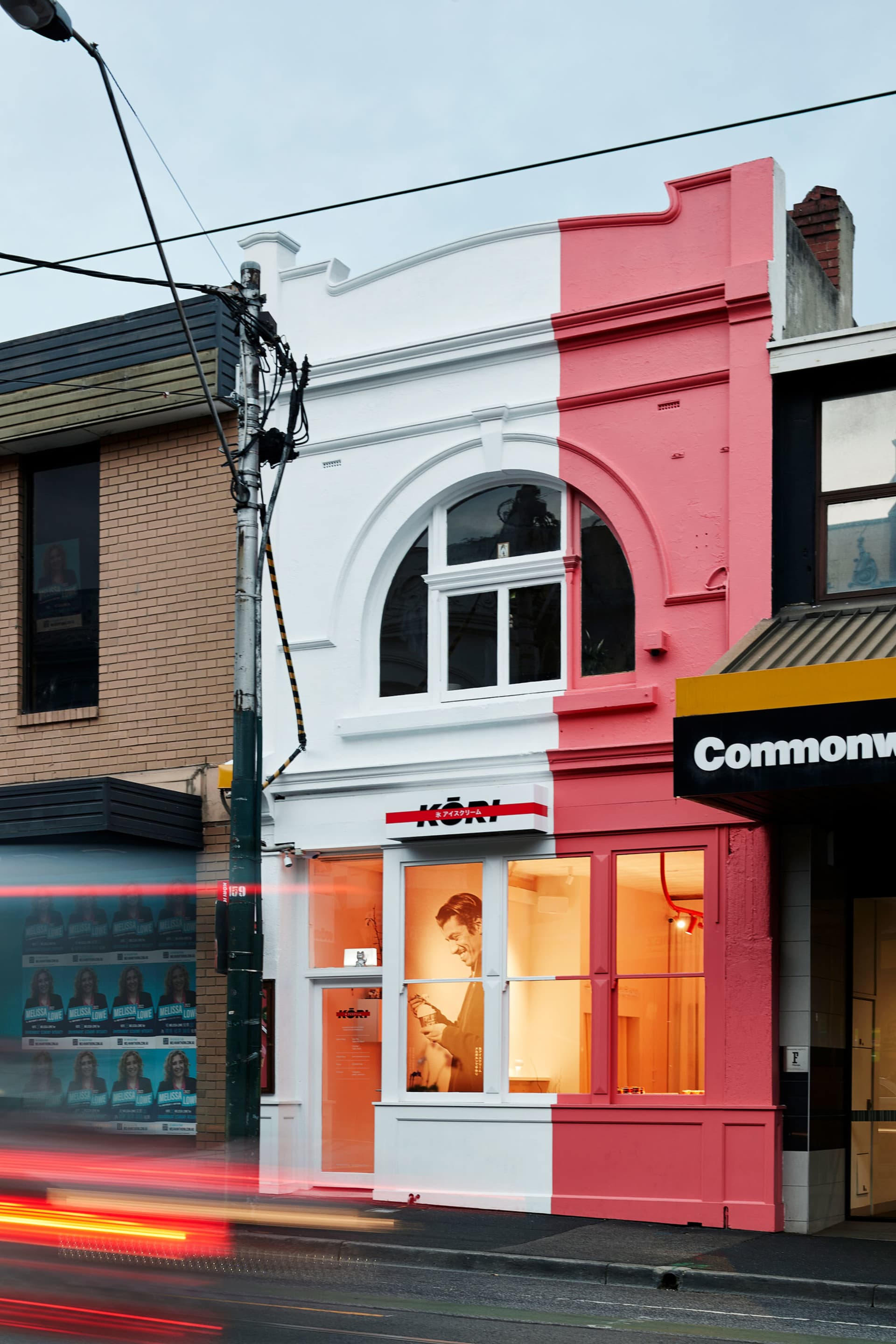 A storefront with pink and white colors, featuring a large arched window and interior lighting.