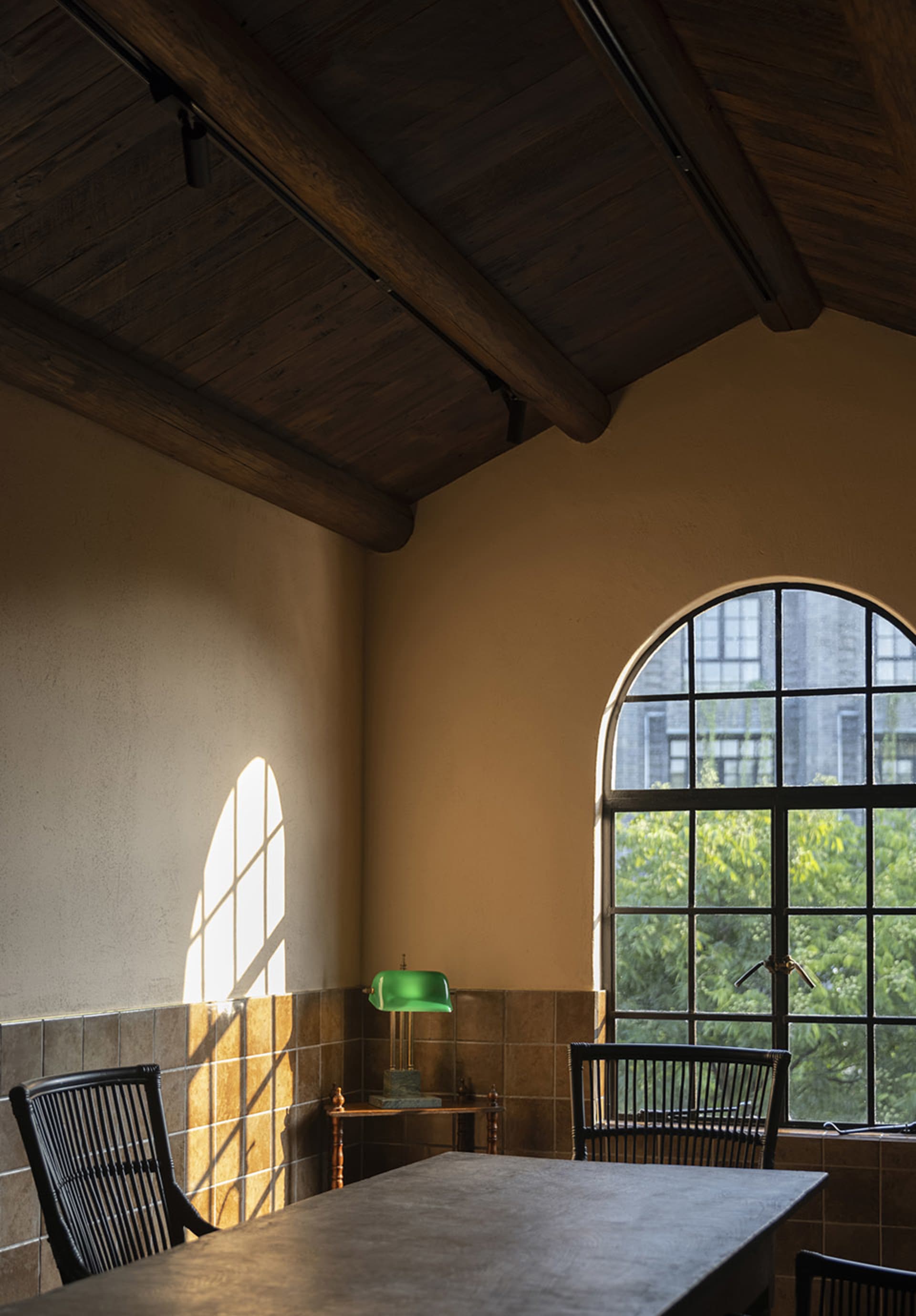 An industrial-style office space with wooden paneling, showcasing a green lamp on a table and a window with an arched design.
