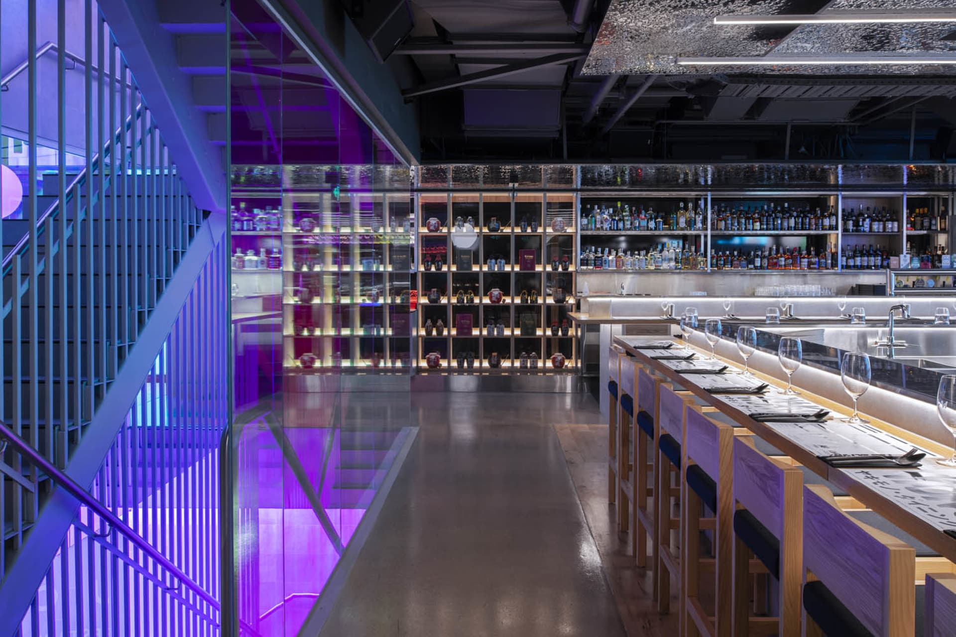 A modern restaurant interior featuring glass walls, concrete flooring, and wooden seating.