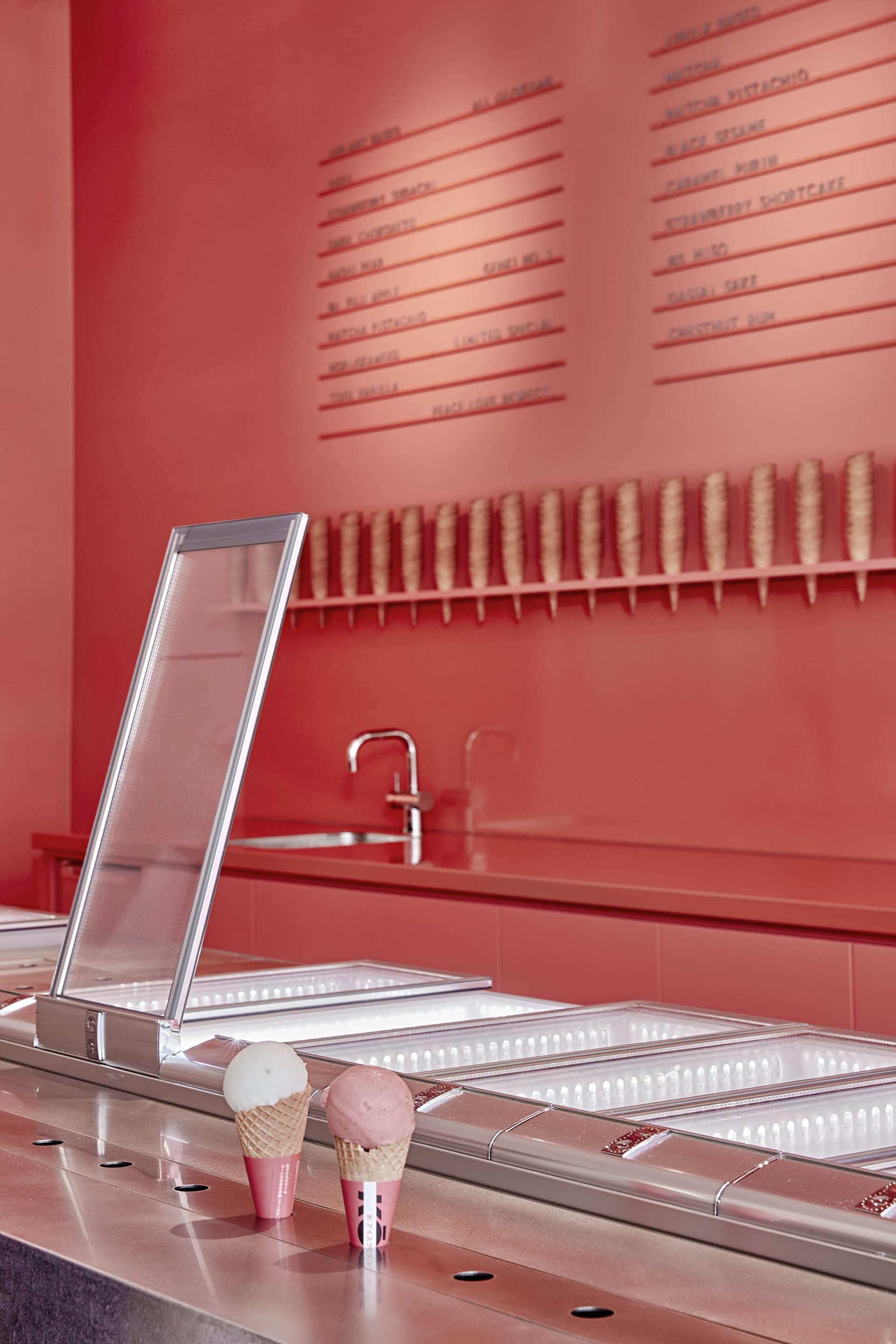 A modern restaurant interior with a sleek metallic counter top featuring an ice cream display and menu behind it.