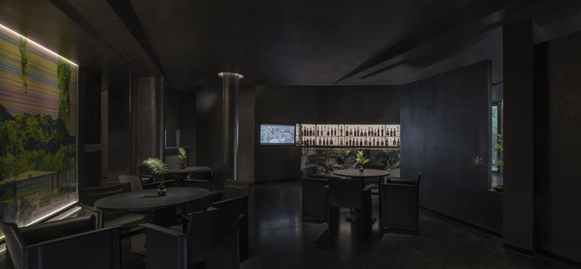Modern restaurant bar featuring a black metallic wall, sleek furniture, and a display of bottled beverages and green plants.