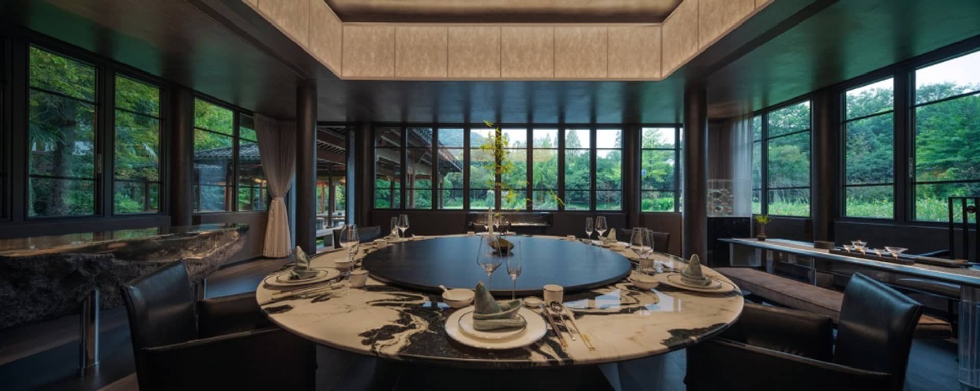 圓形餐桌搭配大理石桌面，周圍環繞黑色皮革餐椅，桌上擺設白色餐盤與酒杯。