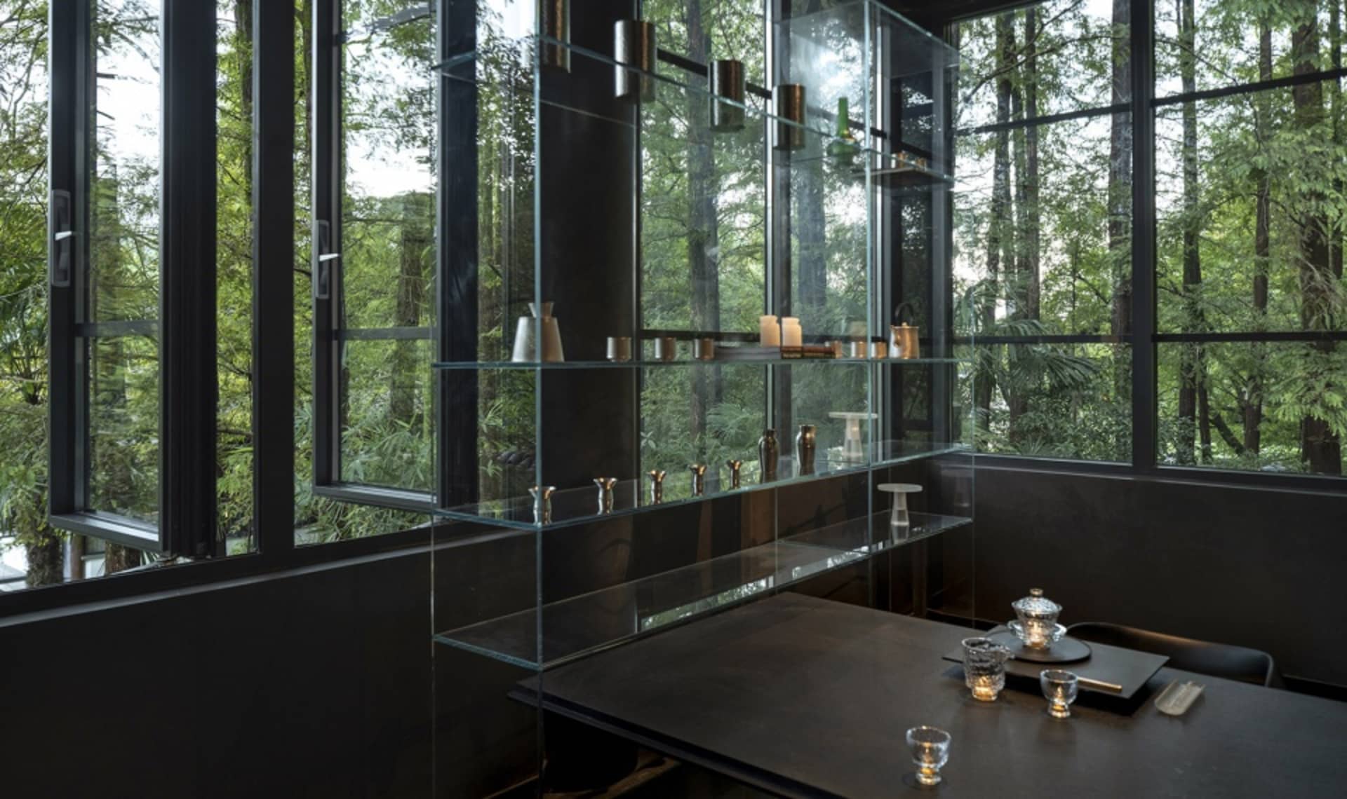 A minimalist restaurant interior with glass walls and wooden accents, featuring sleek metal furniture and a large display cas