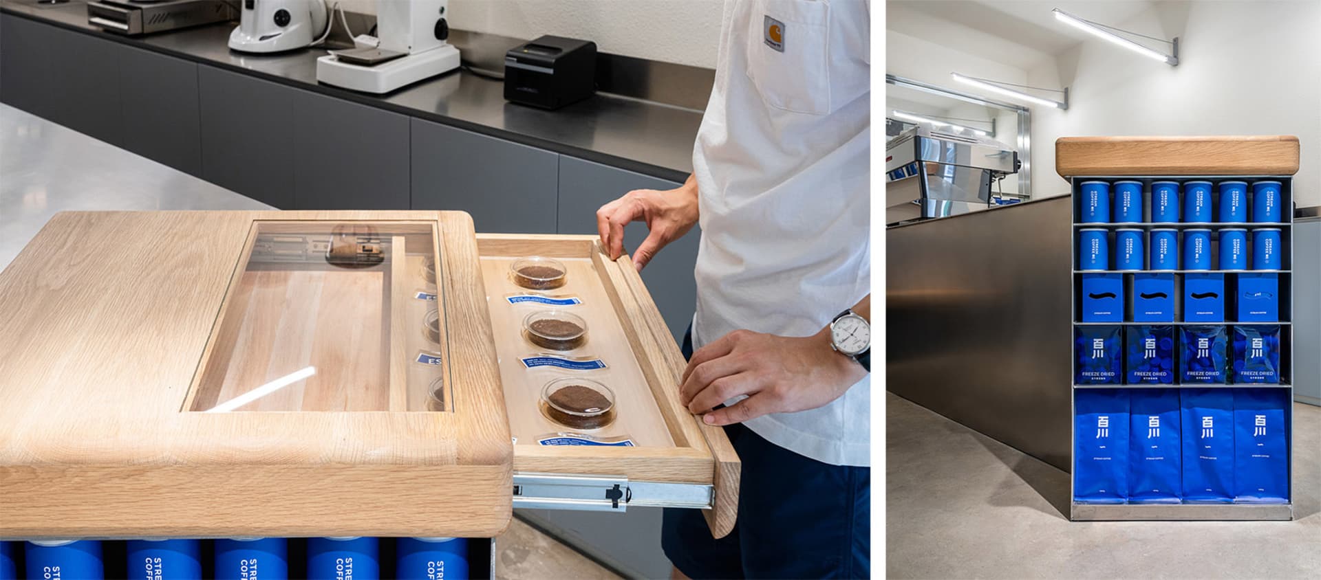 A coffee shop storefront with a wooden table displaying coffee samples, stainless steel countertops, and blue and white packa