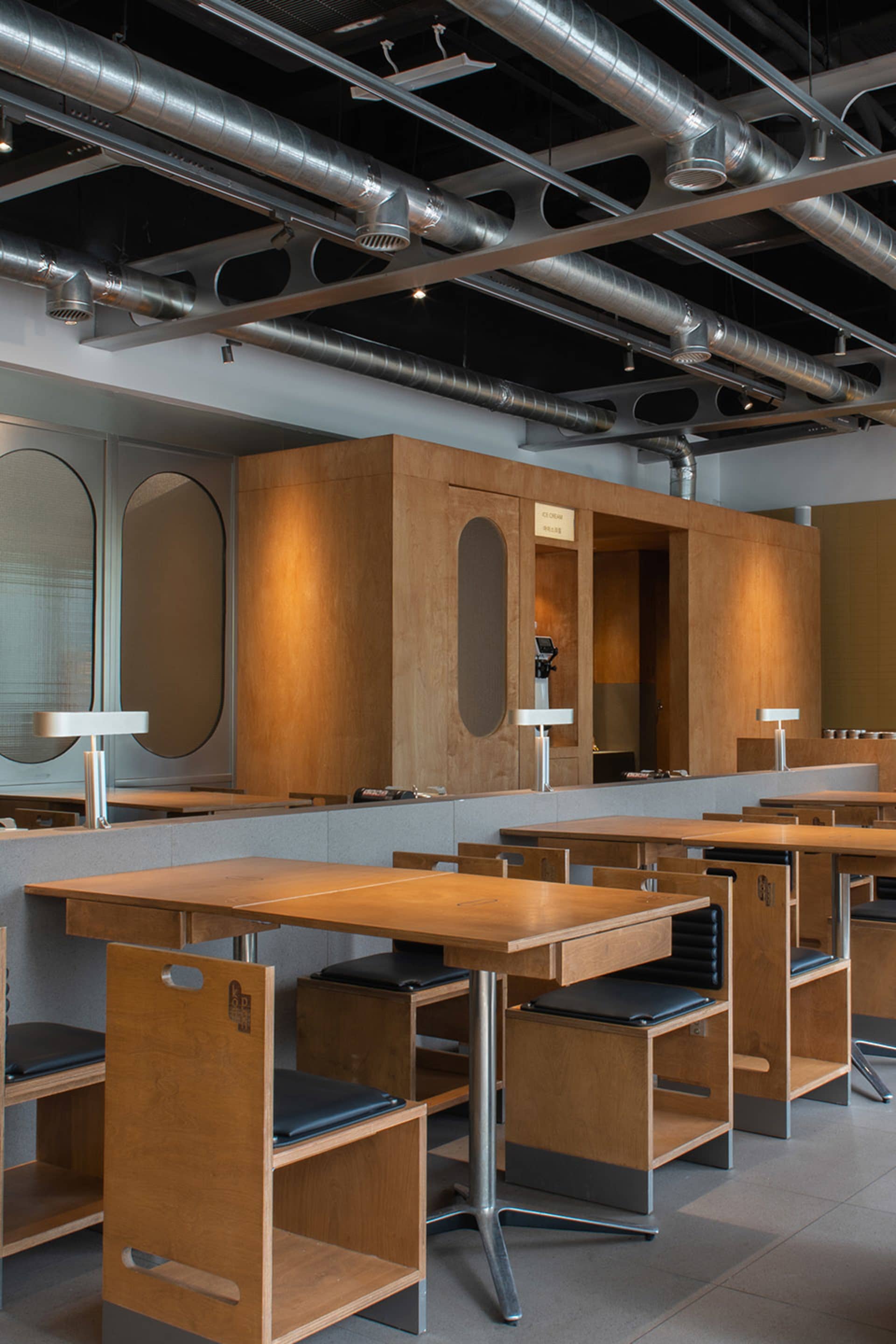 Industrial-themed cafe interior with wooden tables and chairs, under exposed ceiling with exposed pipes and lighting.