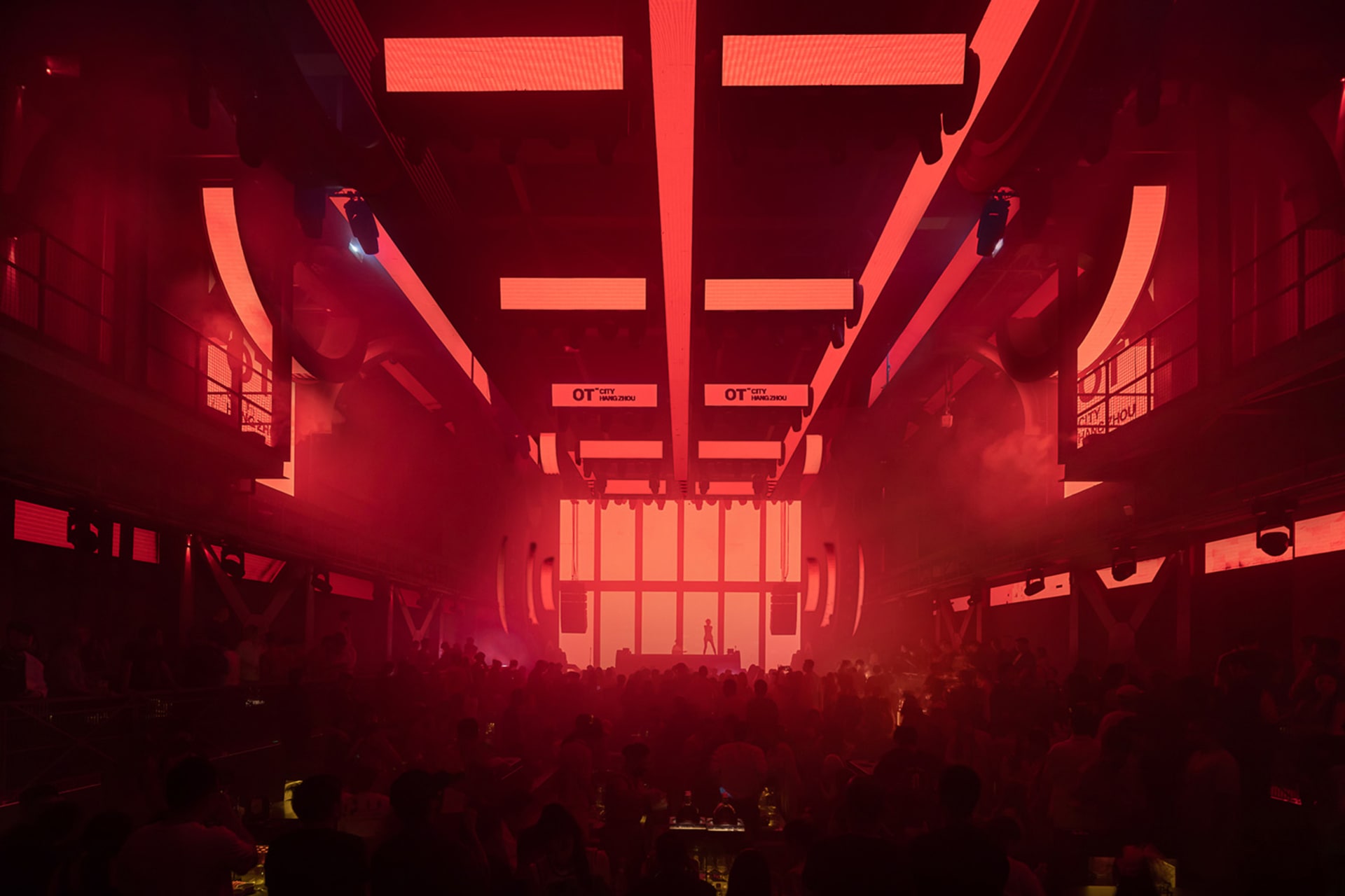 A bustling nightclub illuminated by red lighting and featuring industrial-style steel architecture.
