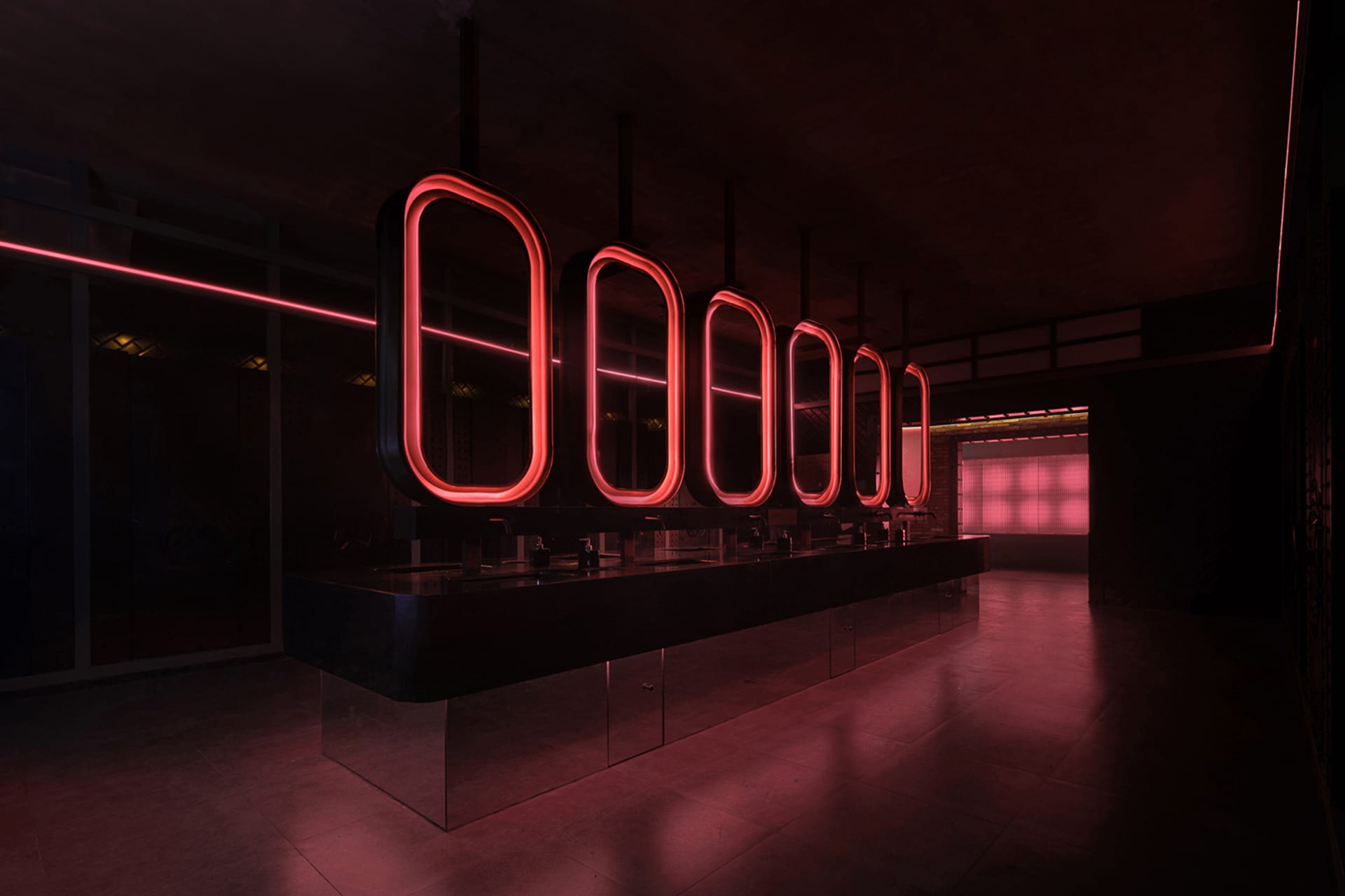 Industrial public restroom with concrete flooring and walls illuminated by neon lights.