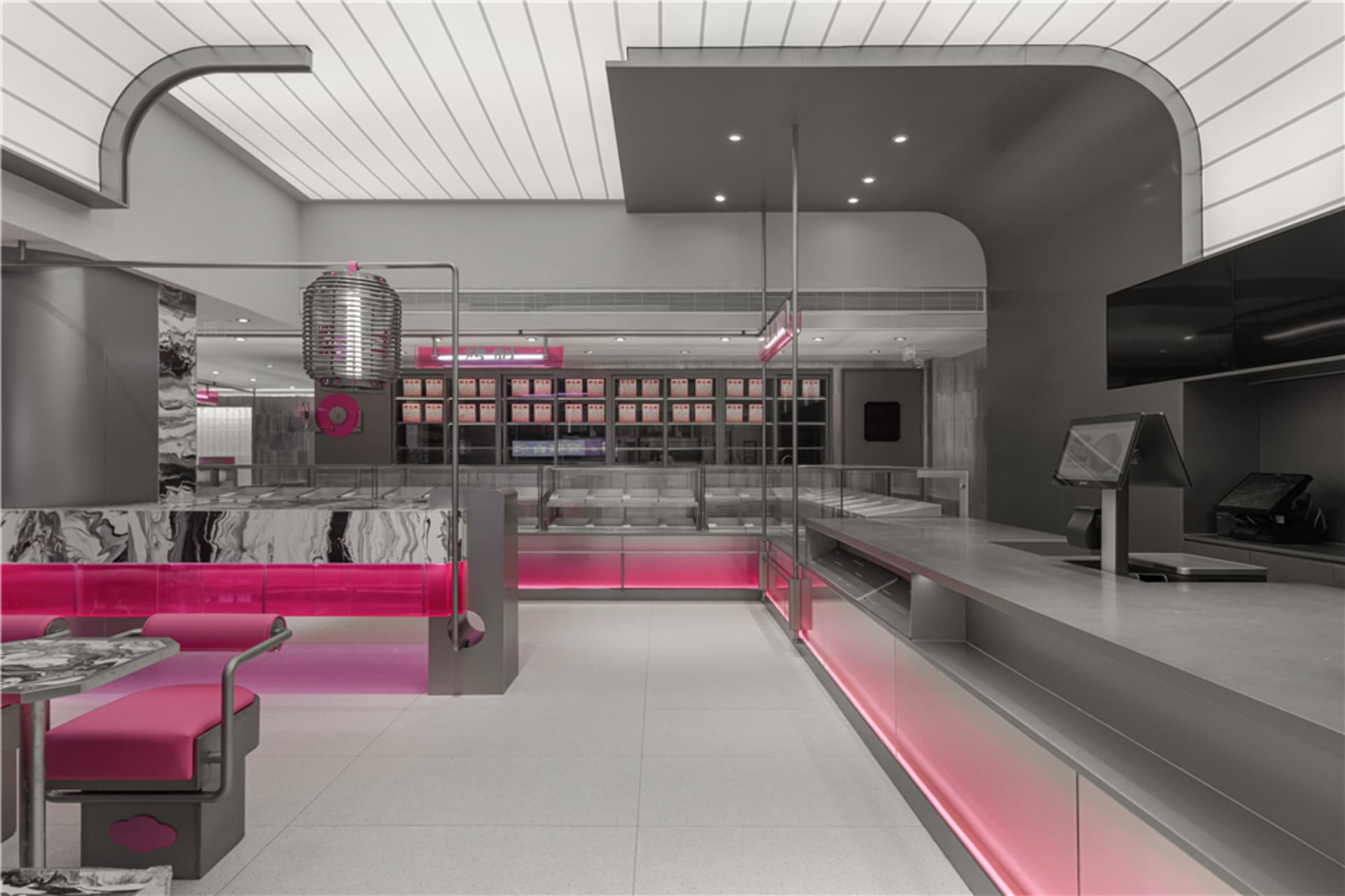 Interior view of a minimalist restaurant with metallic features, marble countertops, pink accents, and pink lighting fixtures