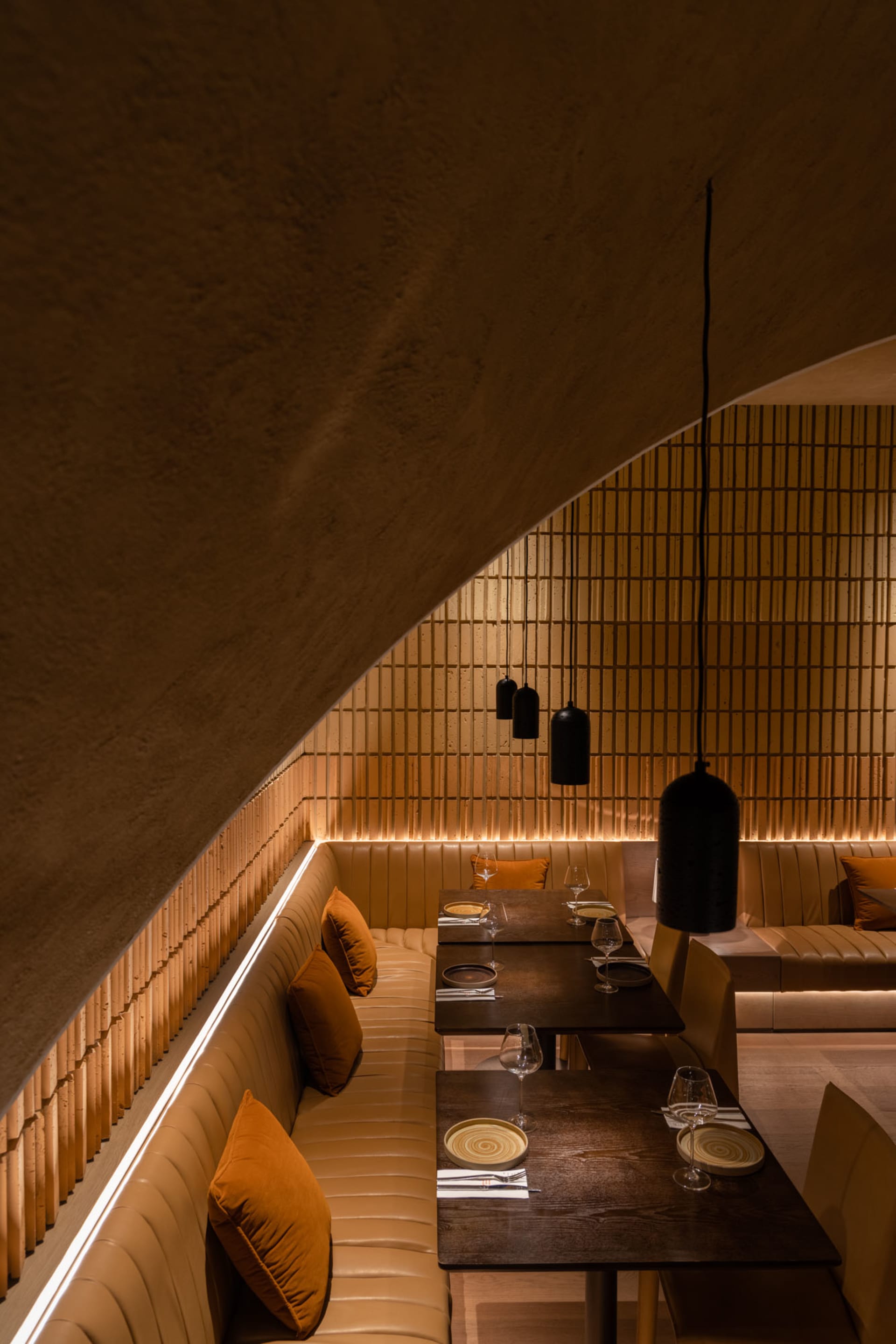 A cozy, industrial-themed restaurant interior with concrete and tiled walls, wooden tables, and plush seating.