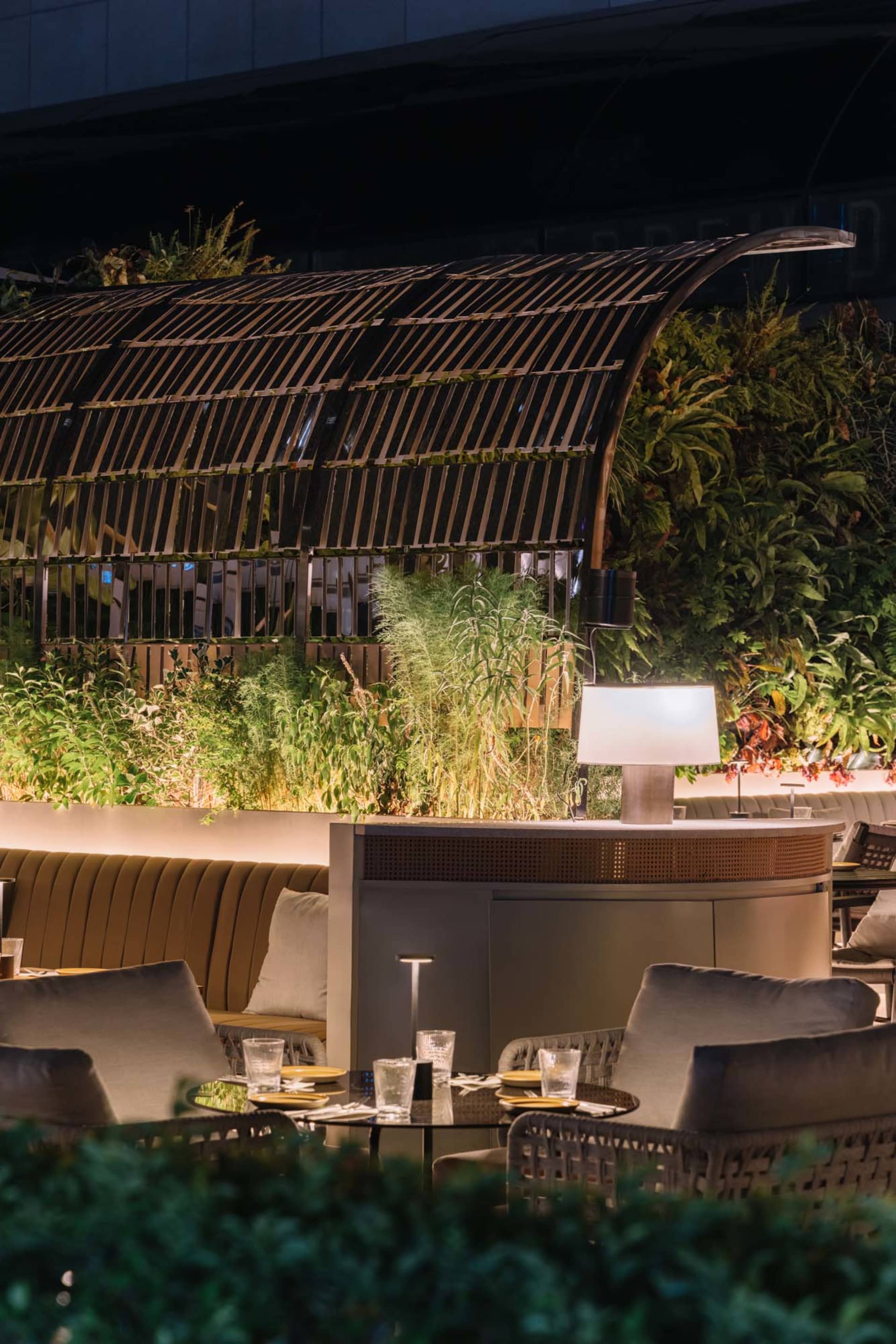 Modern, industrial rooftop bar with metallic structures, glass elements, and concrete flooring.