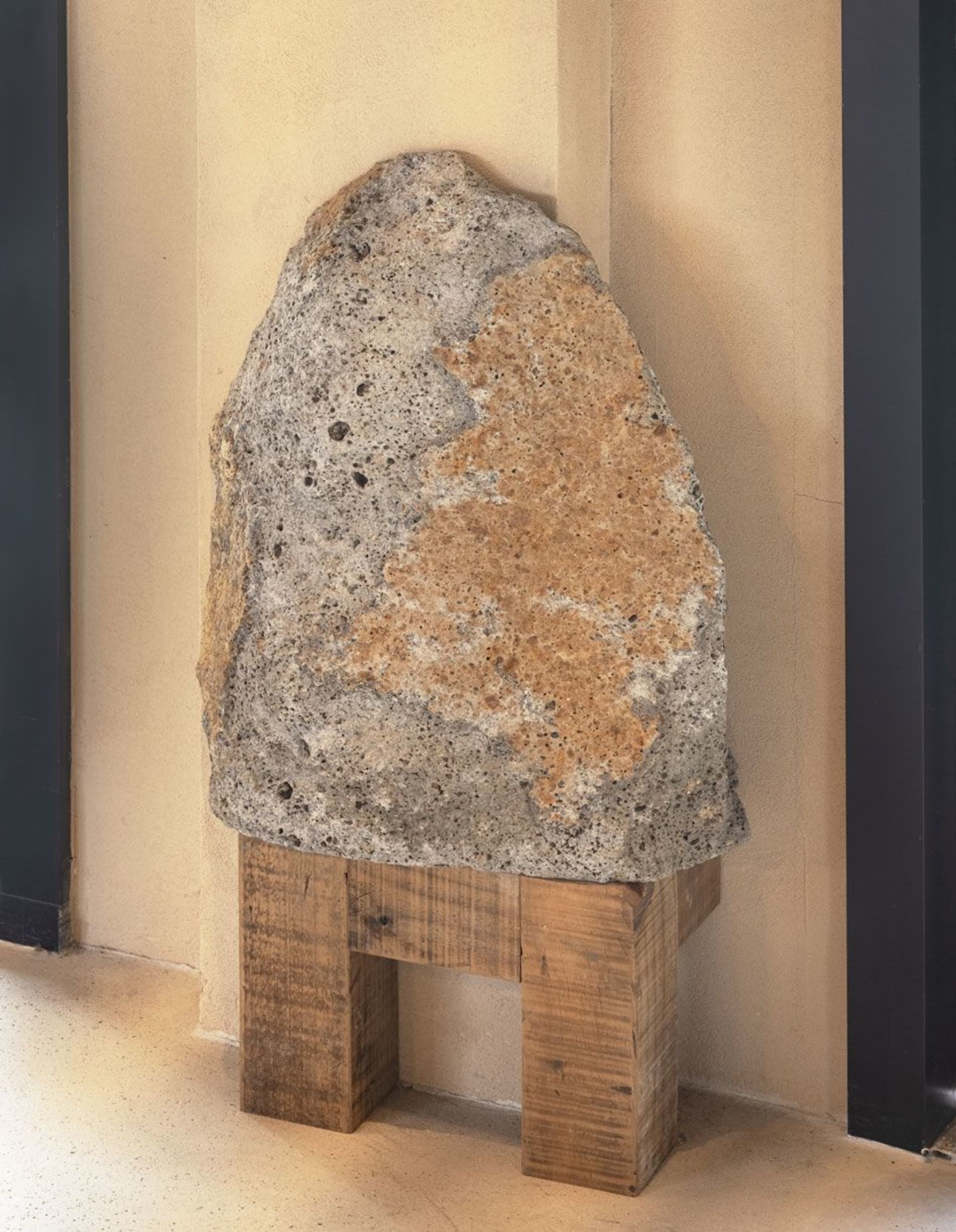 A large, ancient-looking stone block placed atop a rustic wooden frame, resembling a pedestal or stool.