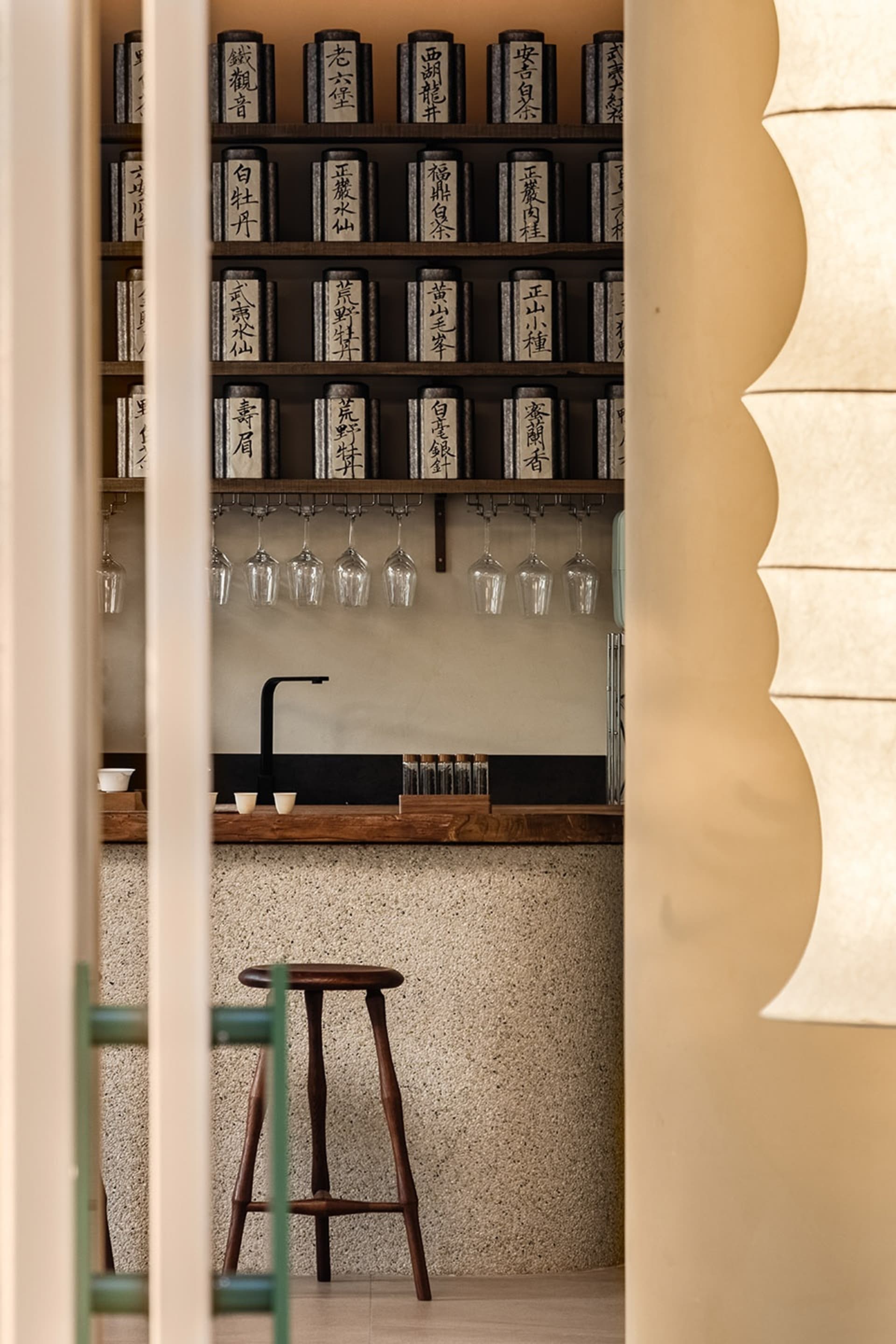 A minimalist tea room interior with wooden stools, glass bottles of tea, and concrete walls.