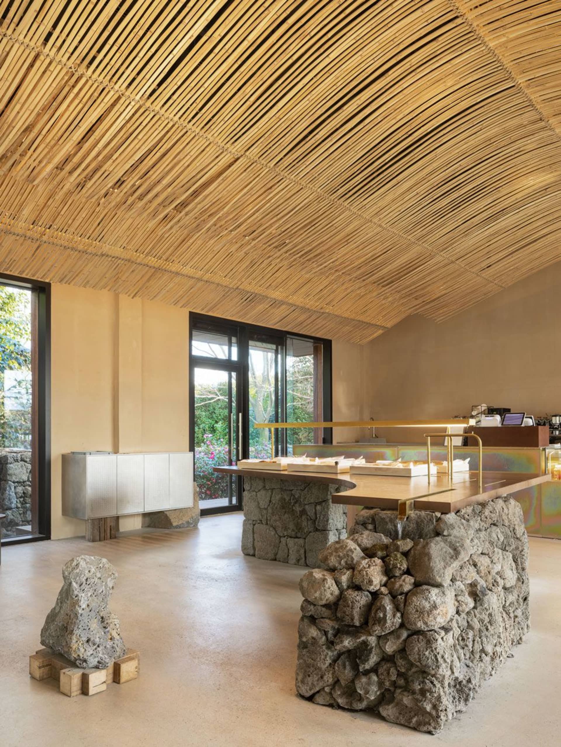A modern cafe with stone and concrete interior, showcasing wooden tables and seating.