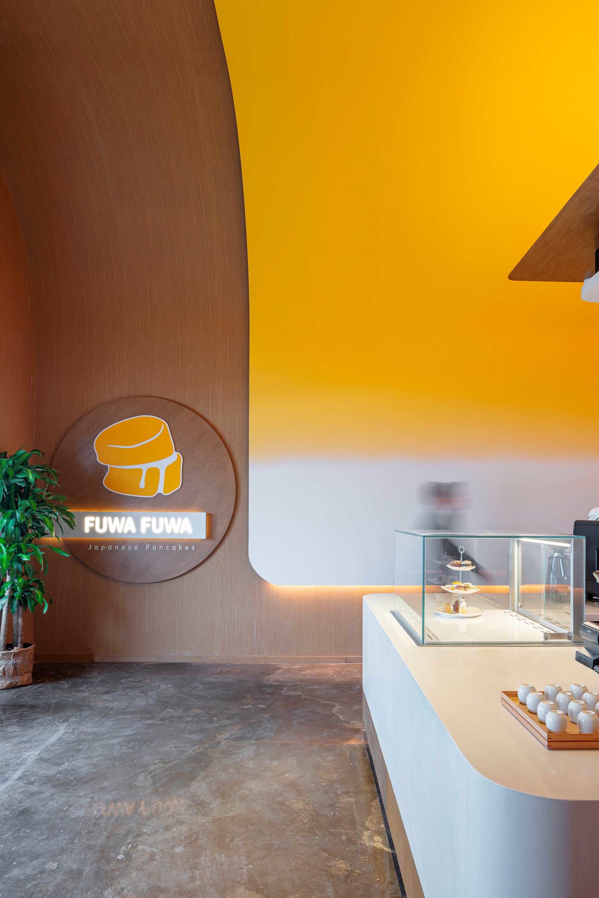 Modern restaurant interior with wooden accents, concrete flooring, and glass display case.