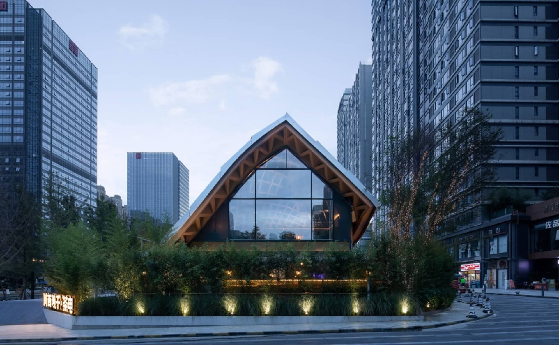 A modern church building with a glass façade surrounded by urban skyscrapers at dusk.