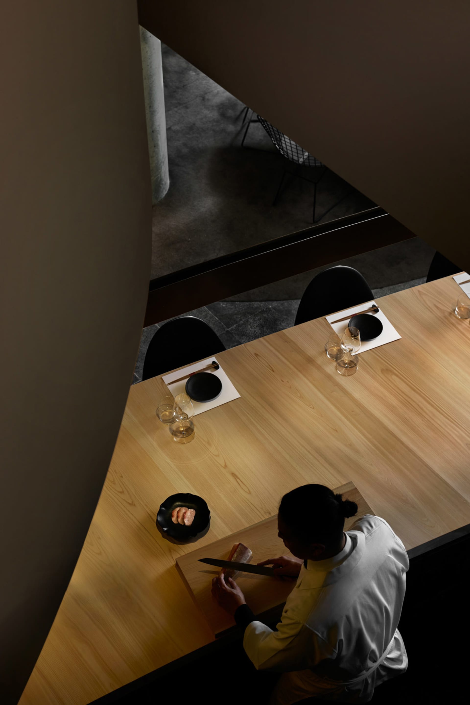 A minimalist restaurant interior with a wooden counter and a chef slicing fish.