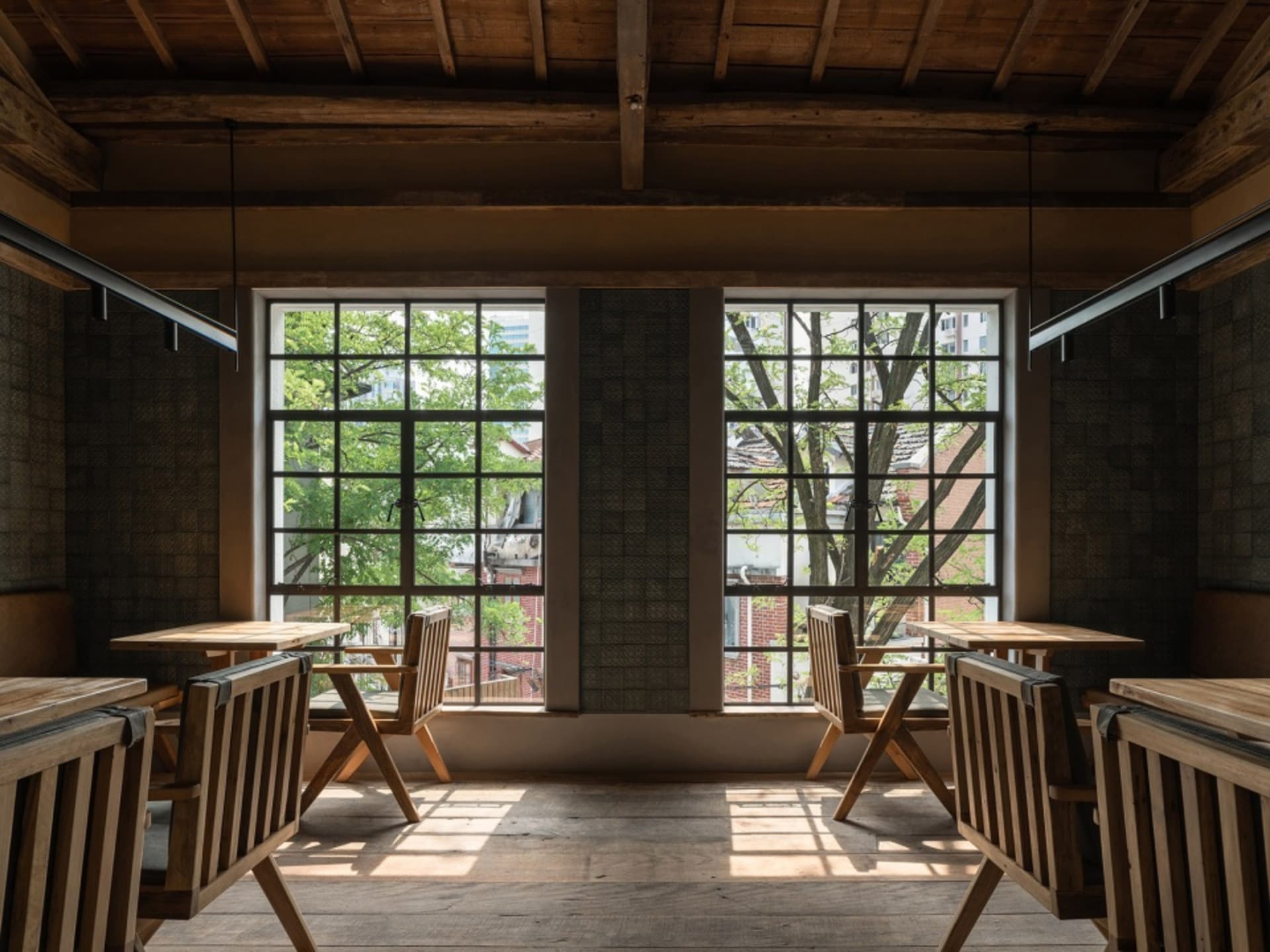 Industrial-style restaurant interior with wooden tables, glass walls, and a view of trees outside