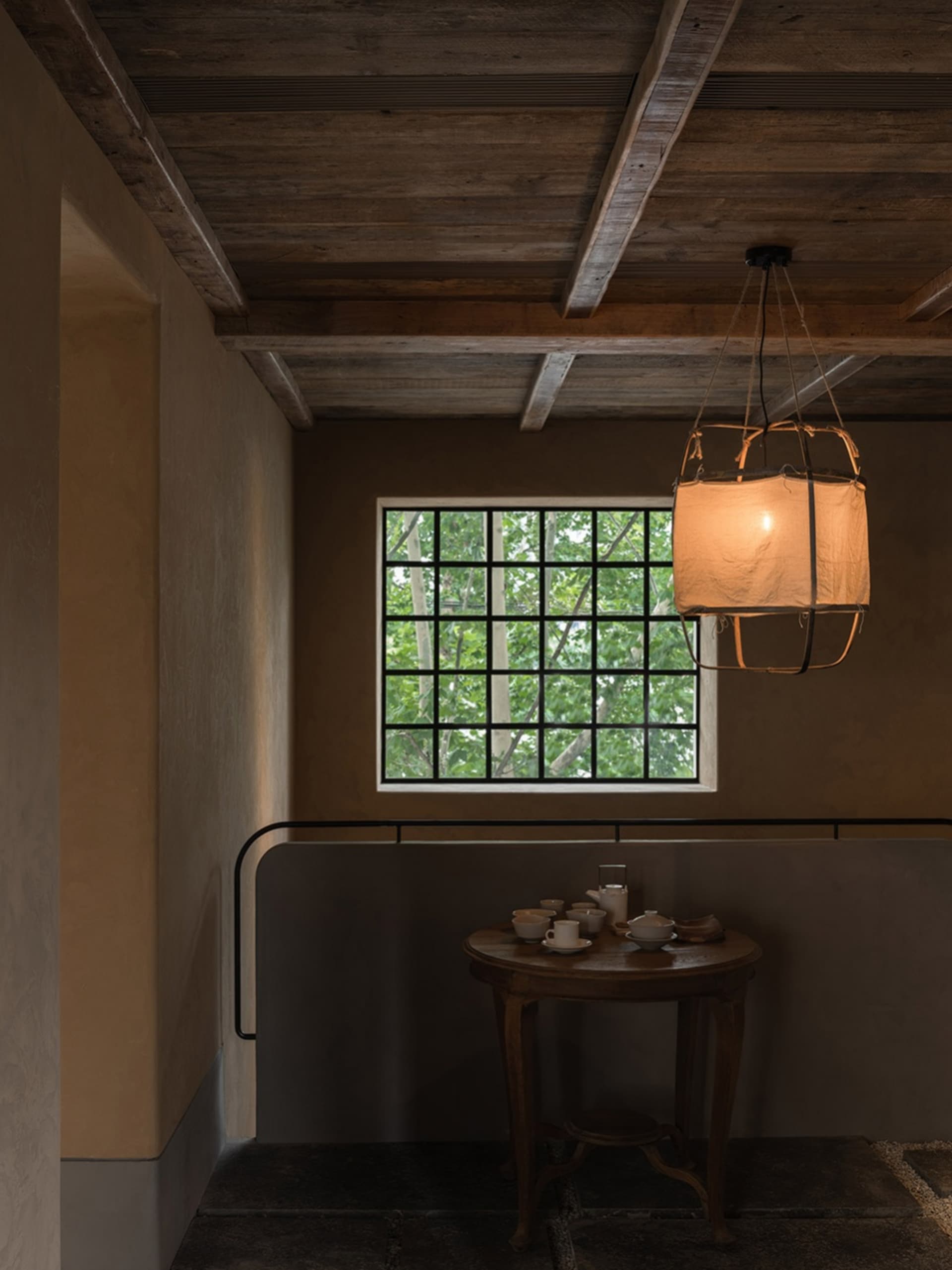 A minimalist interior design featuring a wooden window, table, and chandelier with a warm, soft light.