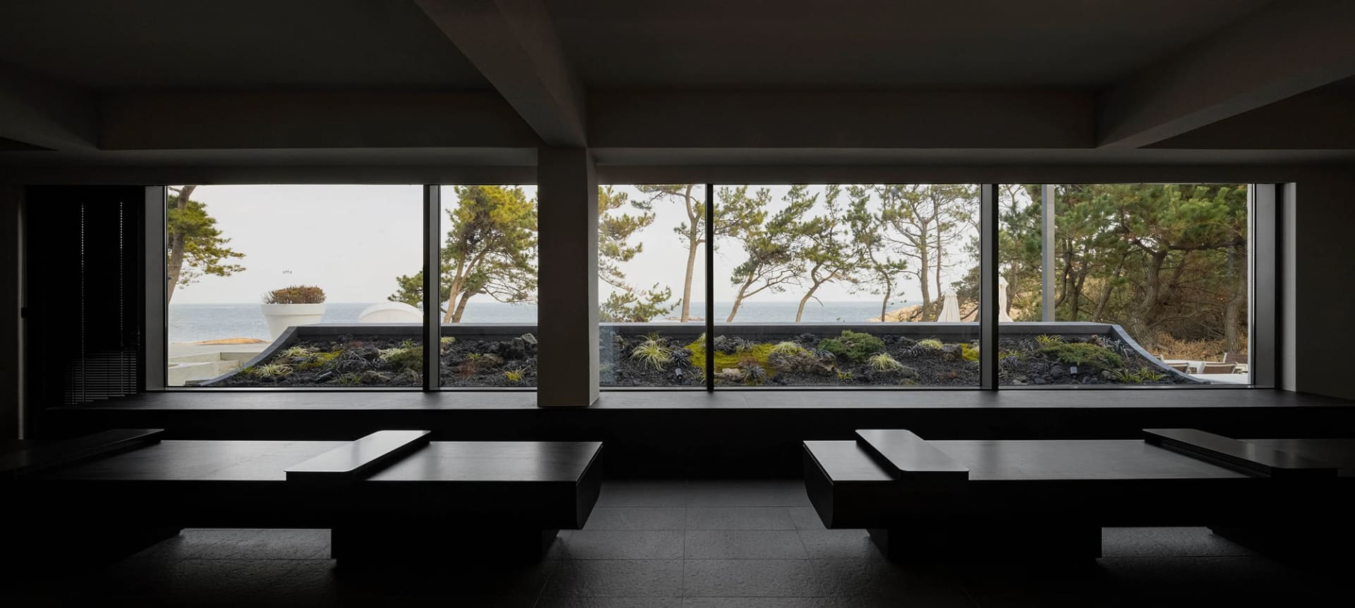 Interior of a modern hotel restaurant with dark wooden tables and view of the ocean through large windows.