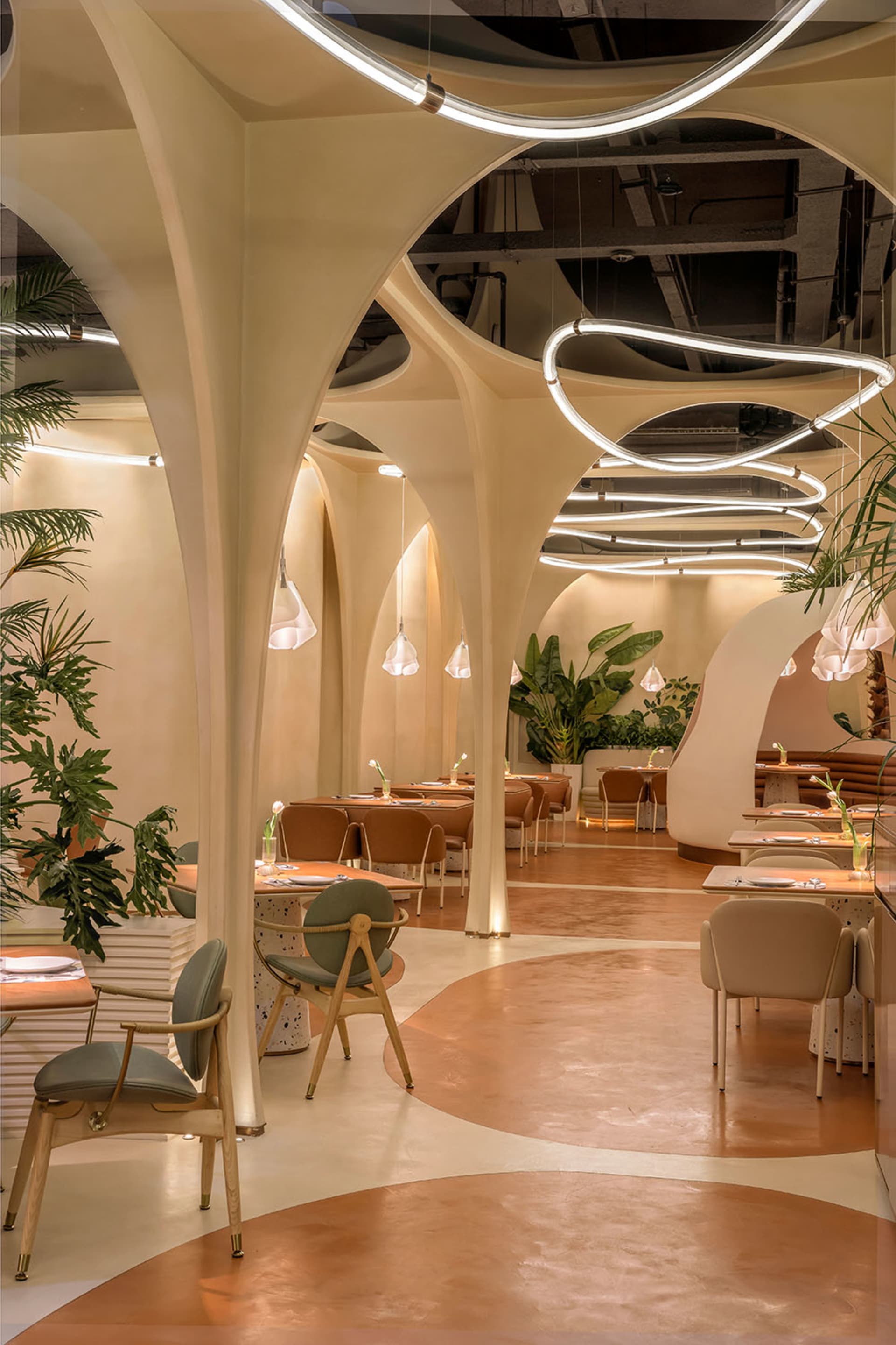 Modern restaurant interior with concrete walls, floral decor, and glass hanging lights.