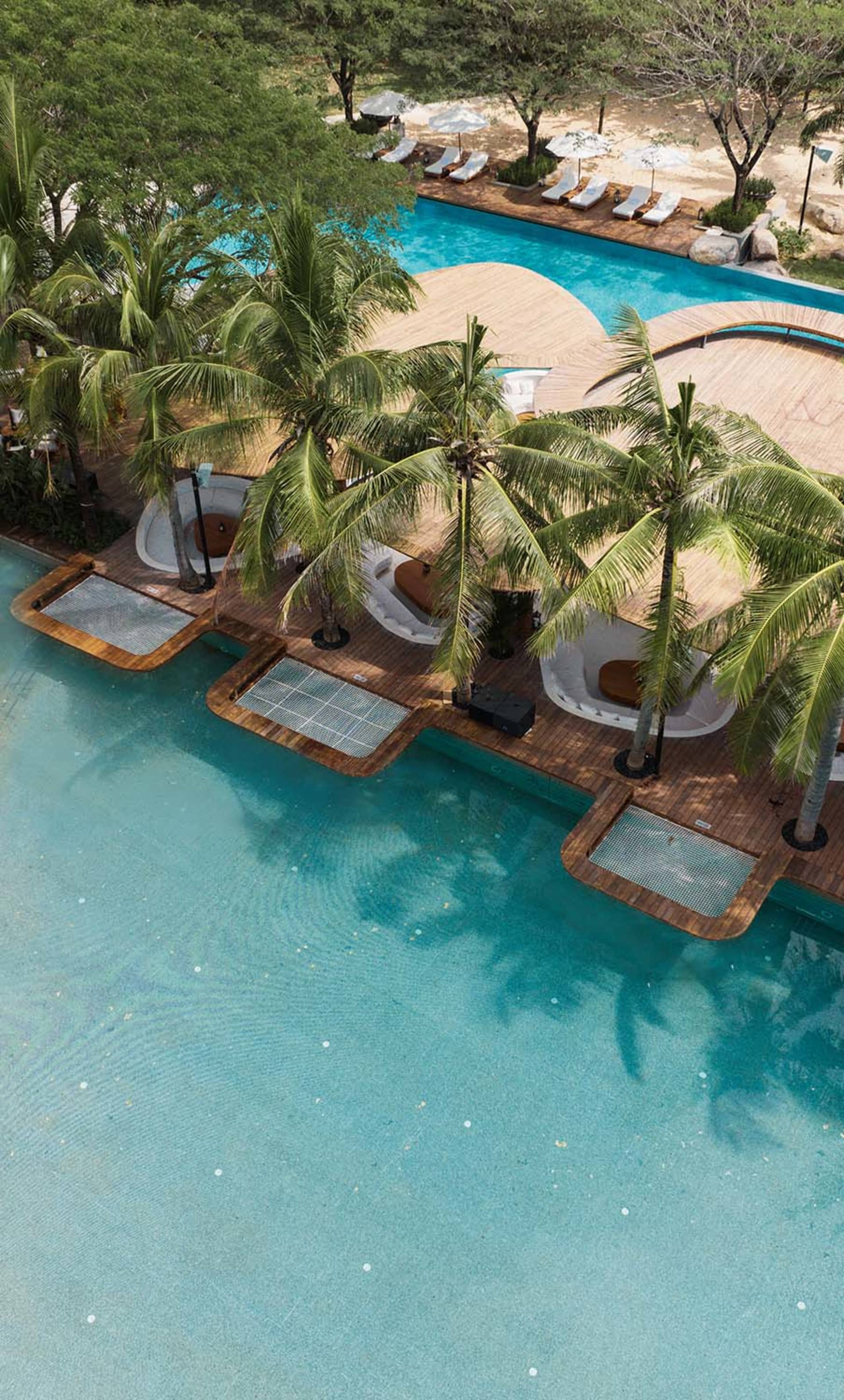 Aerial view of a resort poolside area with concrete structures and palm trees.