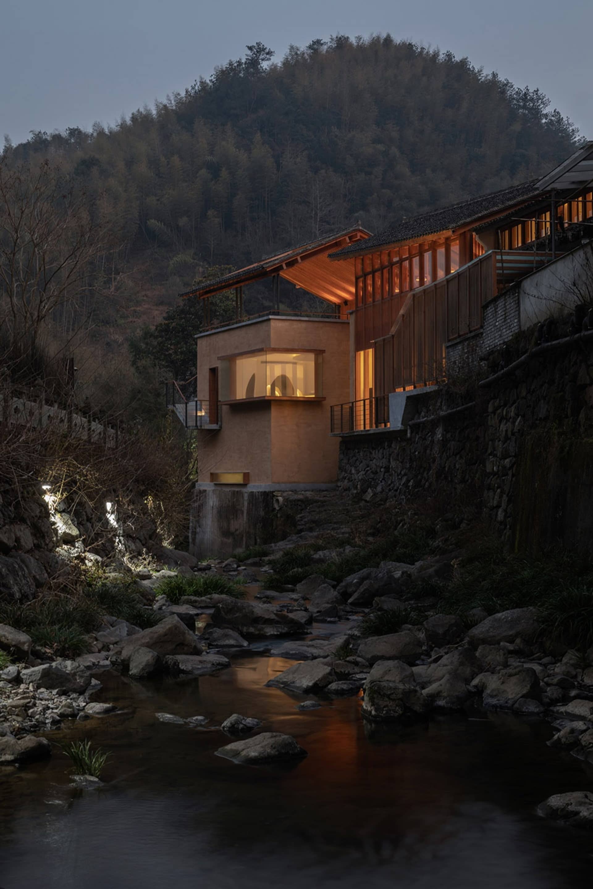 Modern residential house with wooden exterior, glass walls, and concrete foundation at night.