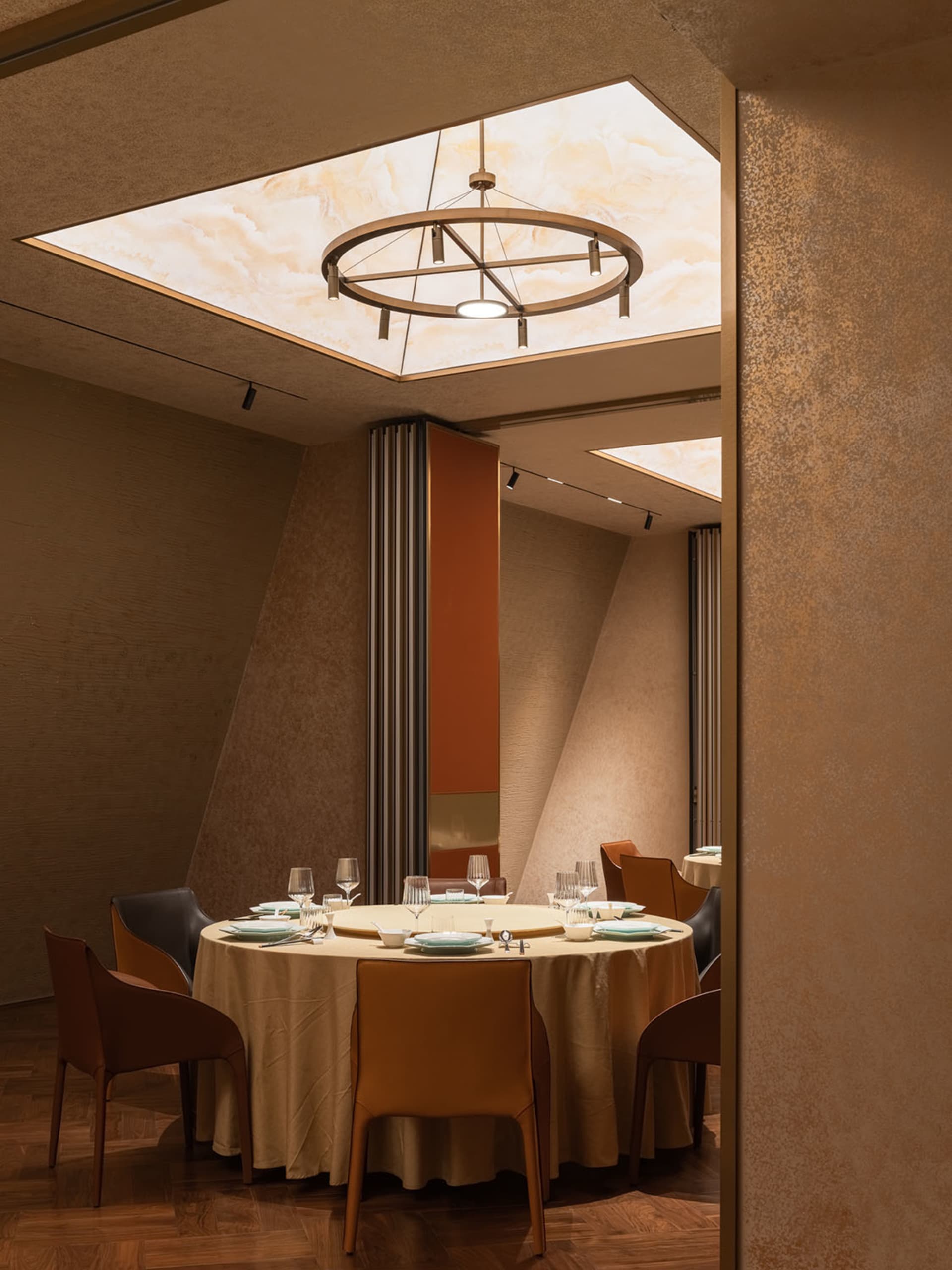 A restaurant interior with textured walls and leather seating, featuring a central circular light fixture with six pendant li