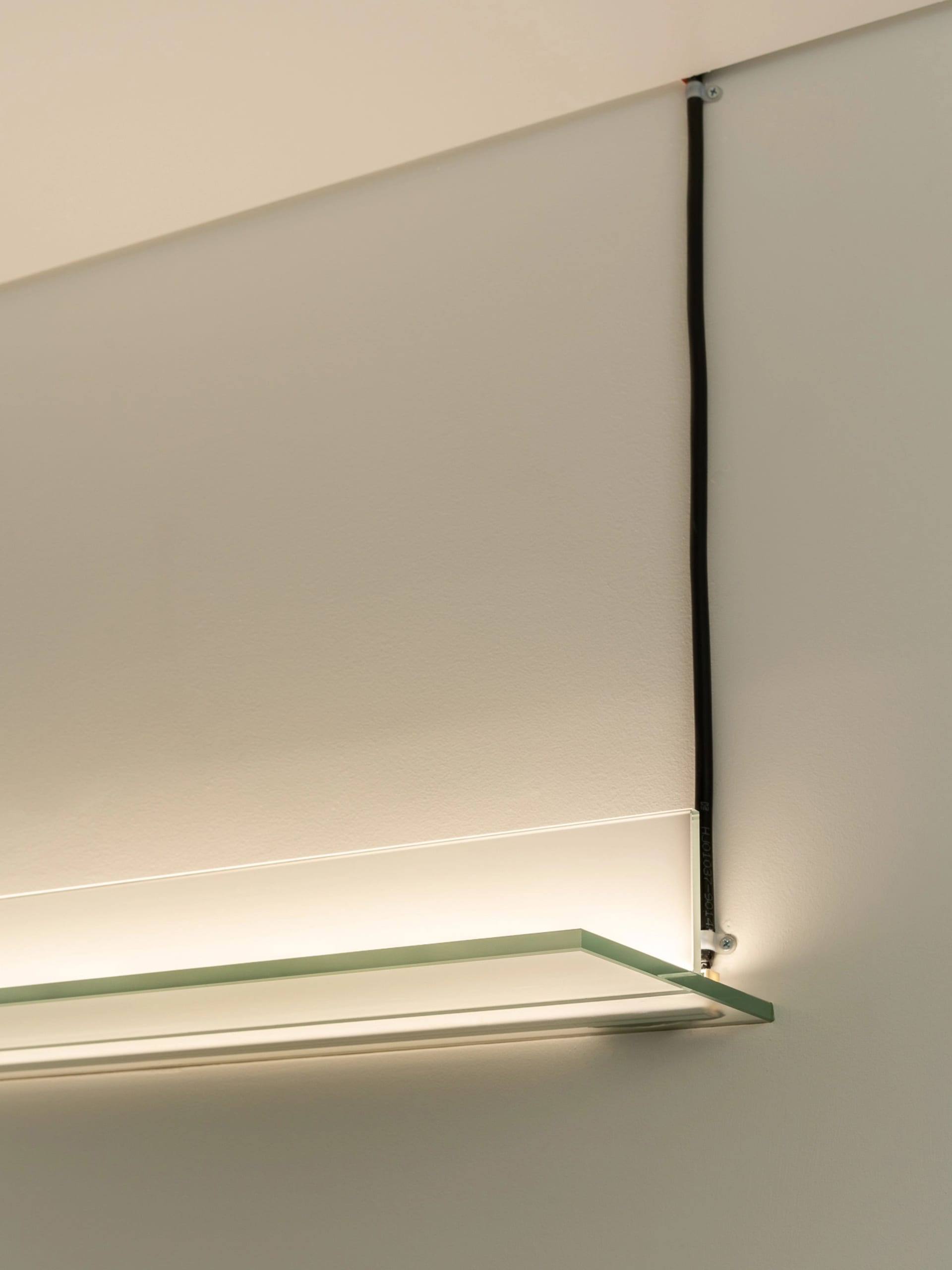 A sleek, modern glass shelf mounted on a wall with a light strip below it.