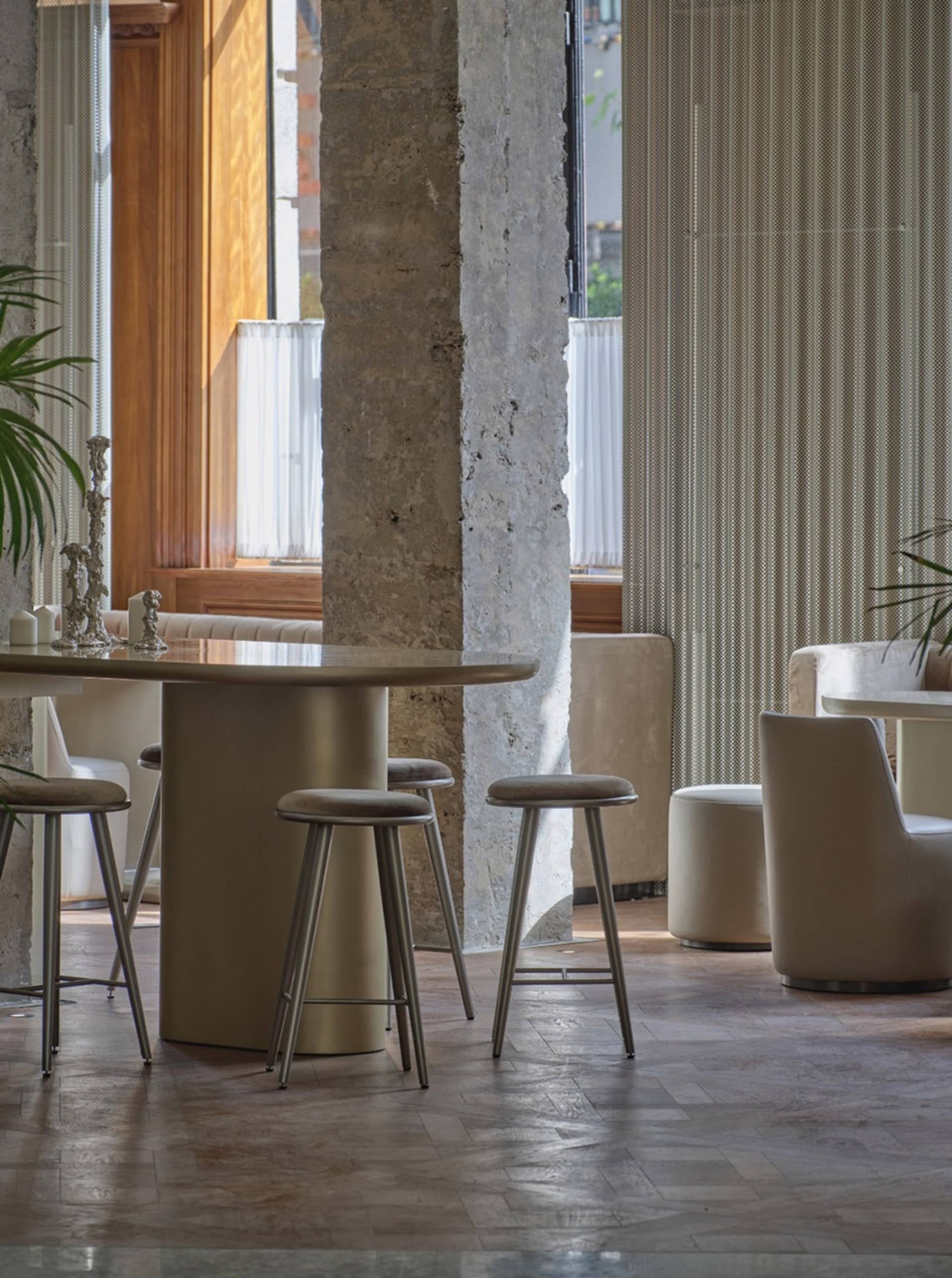 Interior design featuring exposed concrete columns, upholstered seating, and plant accents.