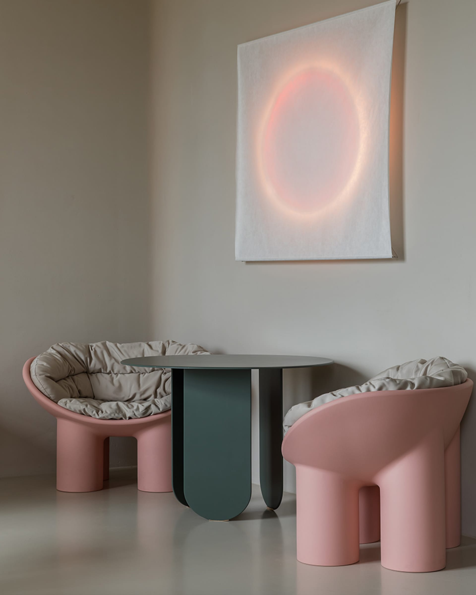 現代休憩區擺放兩張粉紅色曲線塑膠椅，搭配米色坐墊，以及一張小型圓形玻璃桌，呈現簡約風格。