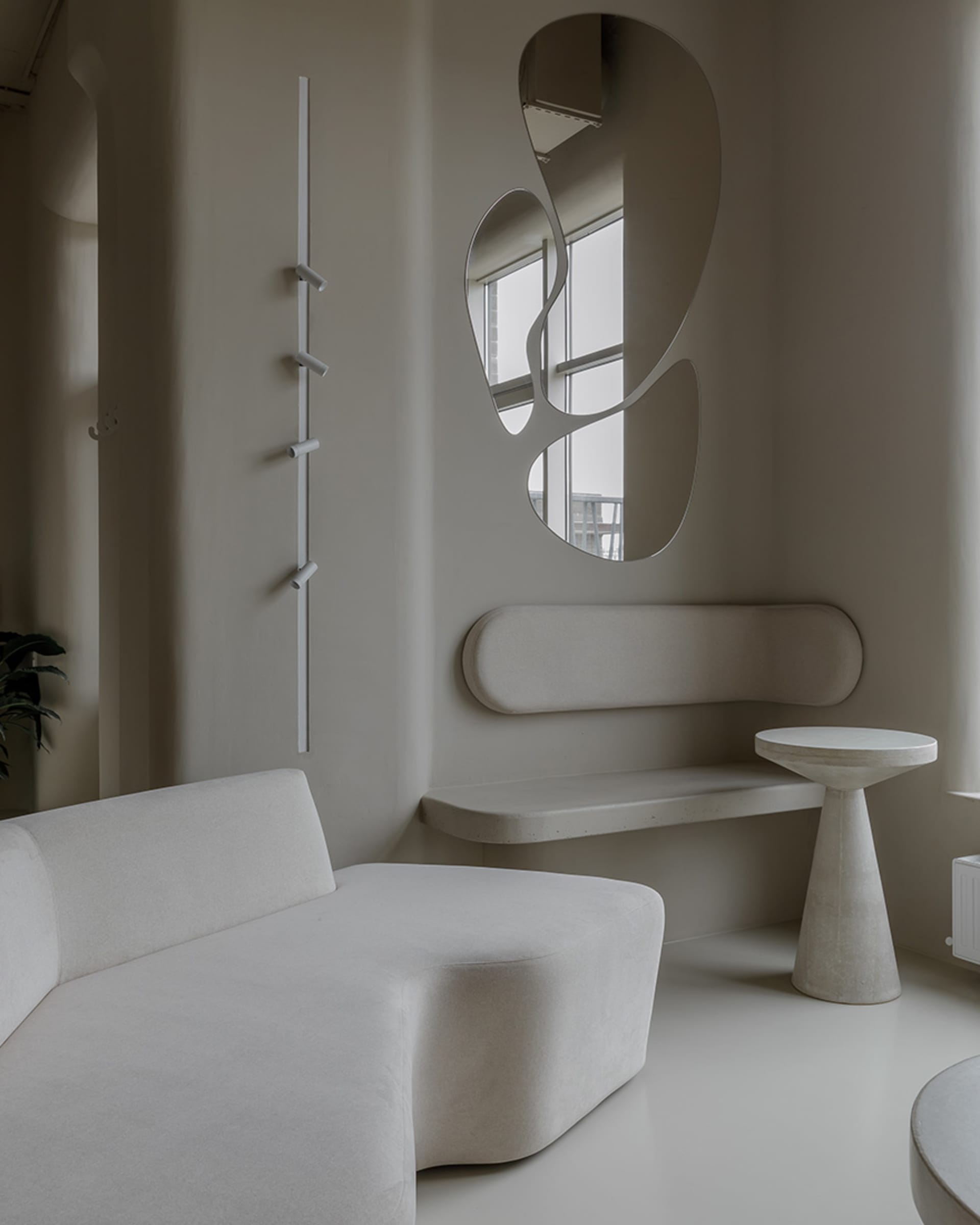 A modern, minimalist living room featuring a beige sofa, abstract wall decor, and round concrete coffee table against a white