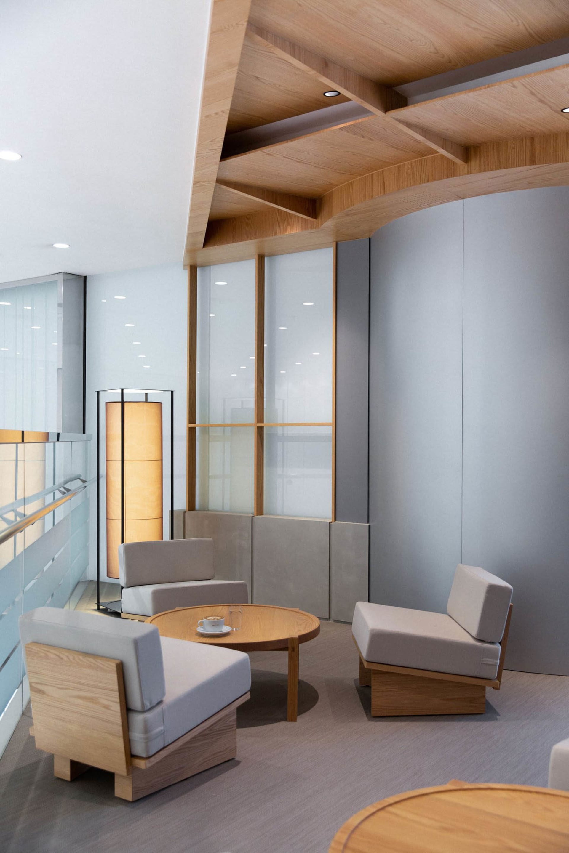 A modern office lounge featuring wooden furniture and a round wooden coffee table with coffee cups and glasses.