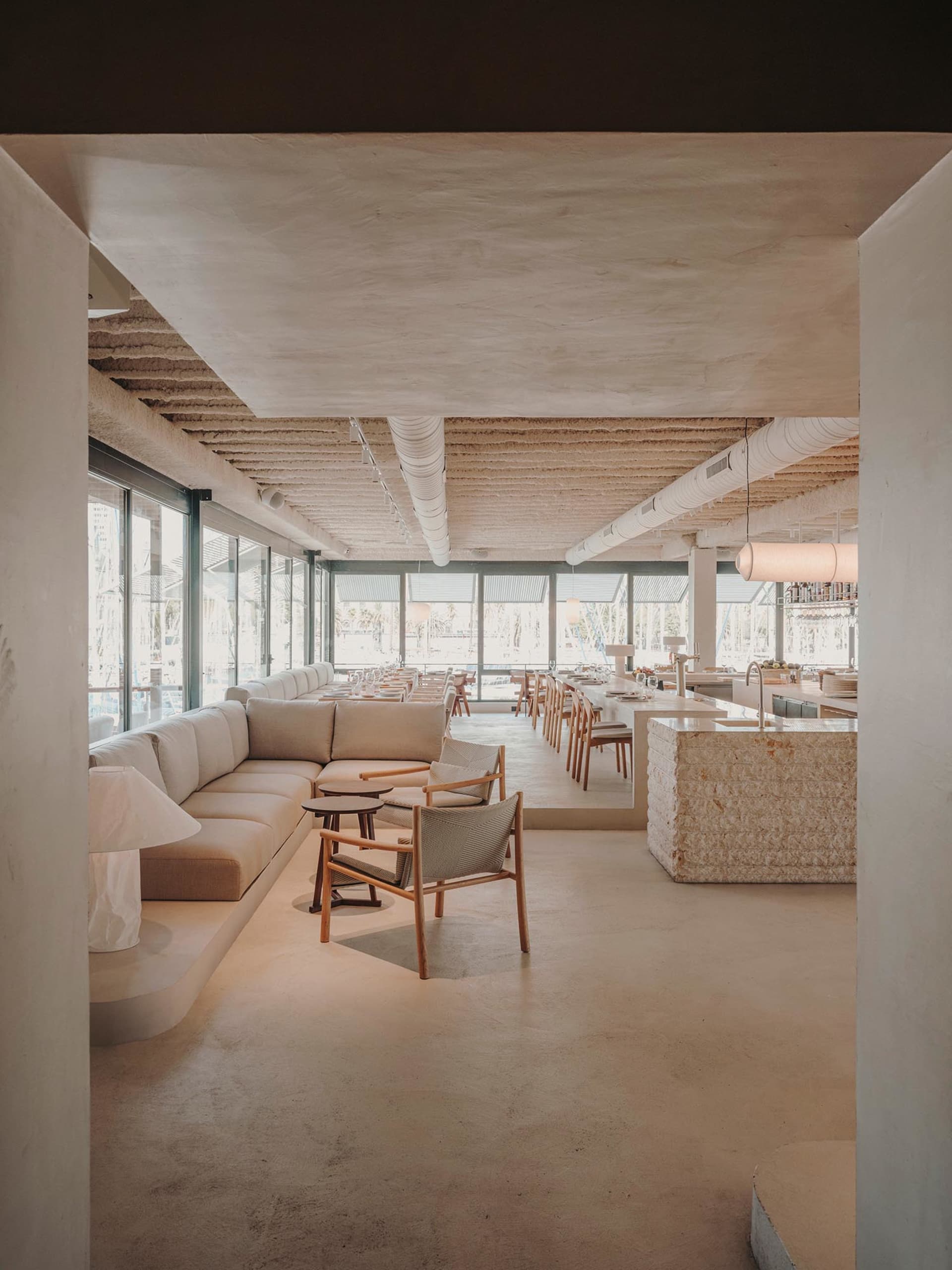 Modern restaurant interior with concrete flooring, large windows, and minimalist furniture.