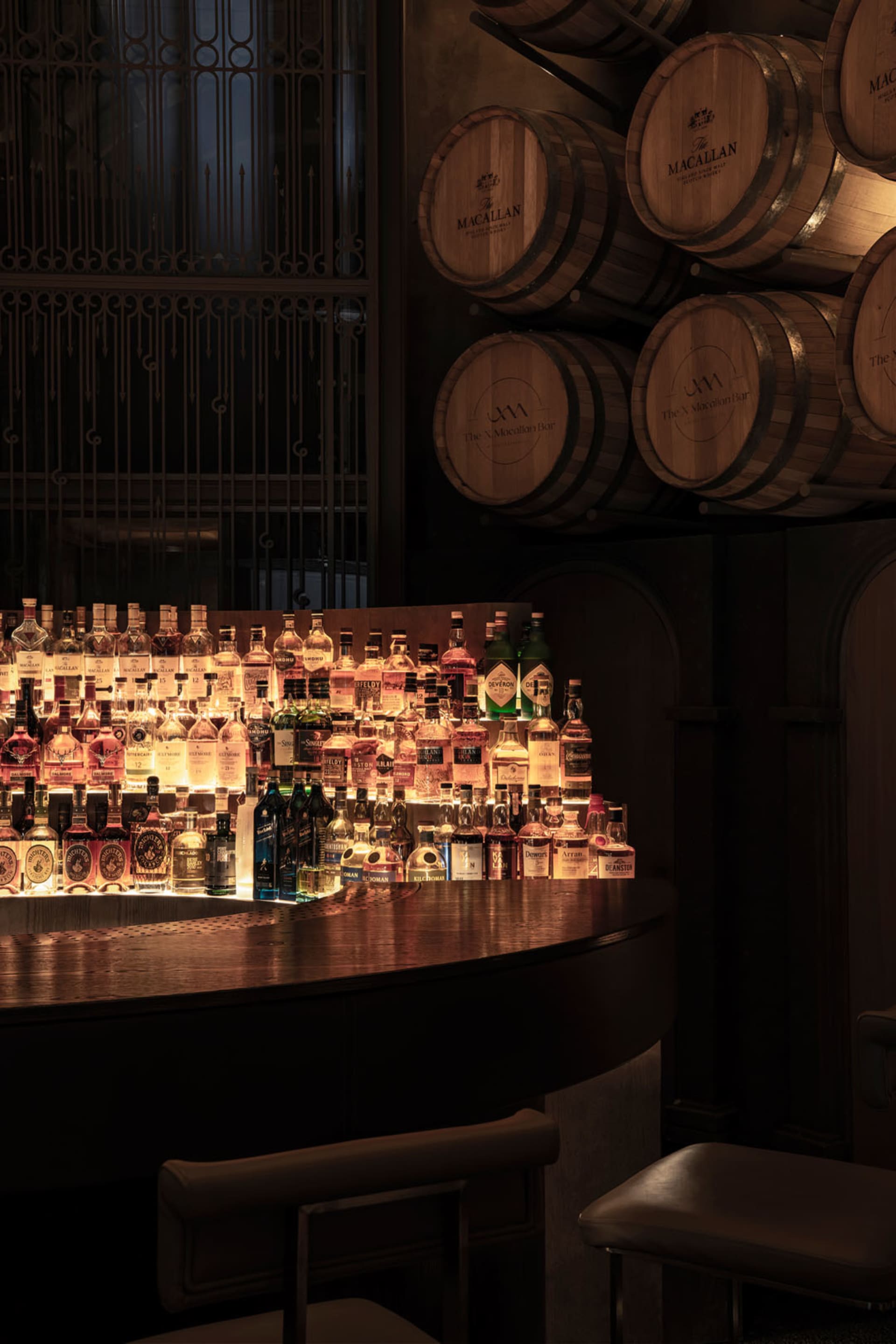 A modern whisky bar with wooden countertops and shelves filled with various bottles and barrels.