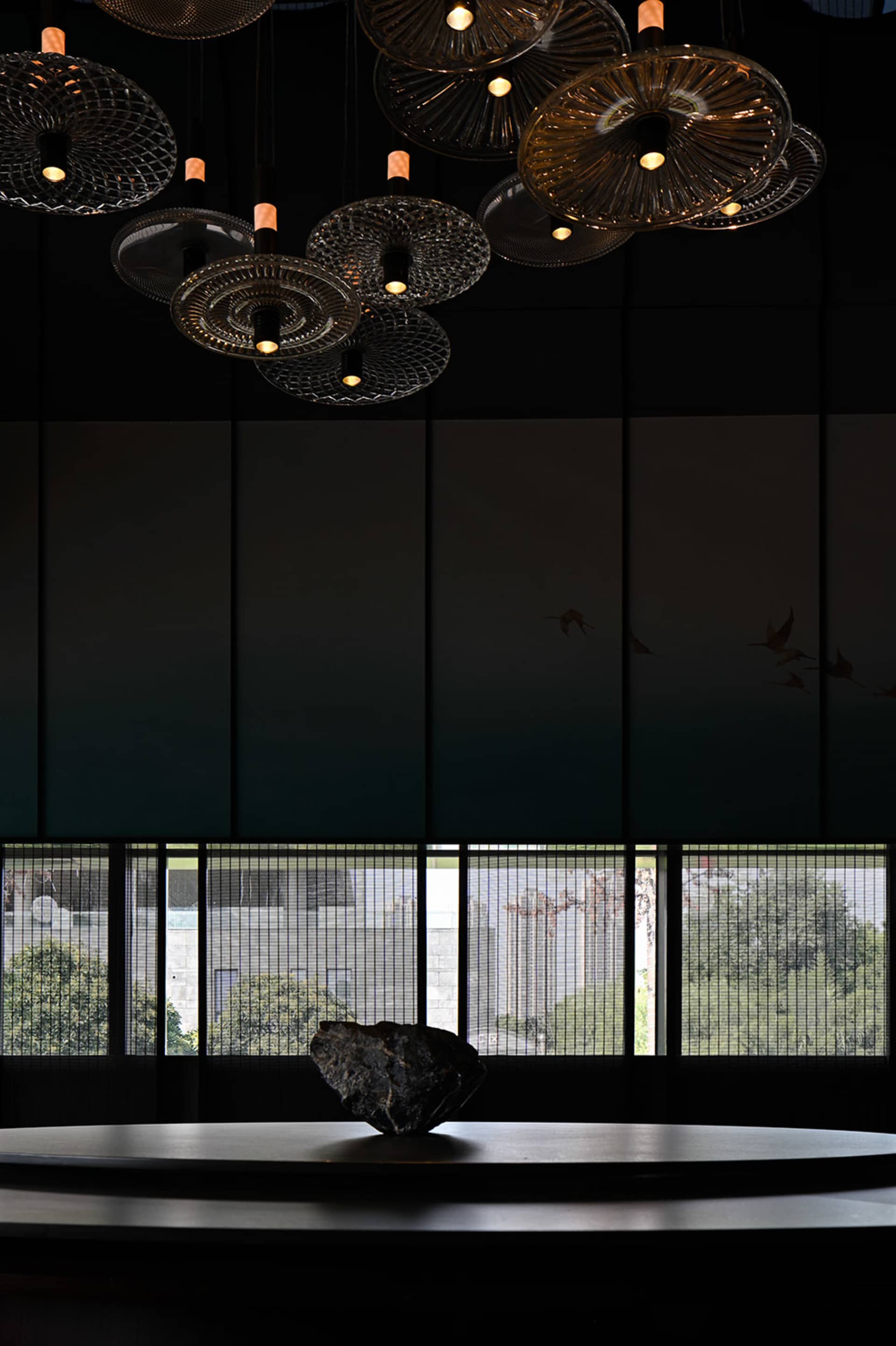An elegant lobby interior with hanging glass light fixtures and a large stone sculpture on a round table.