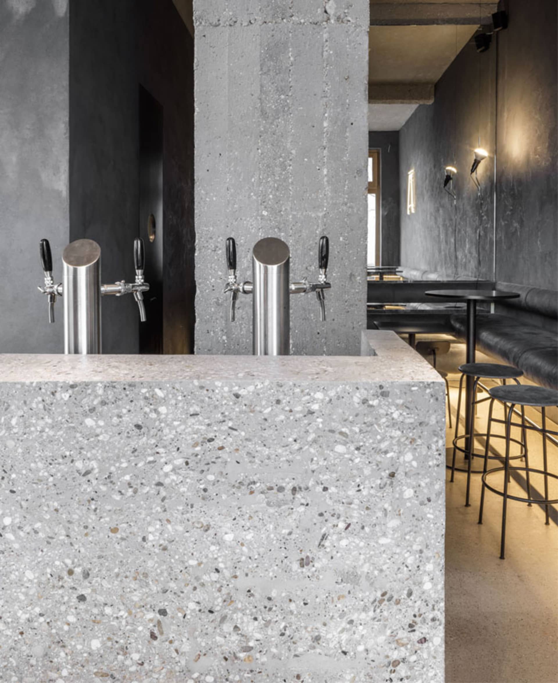 Modern industrial bar with concrete and terrazzo surfaces and stainless steel beer taps.
