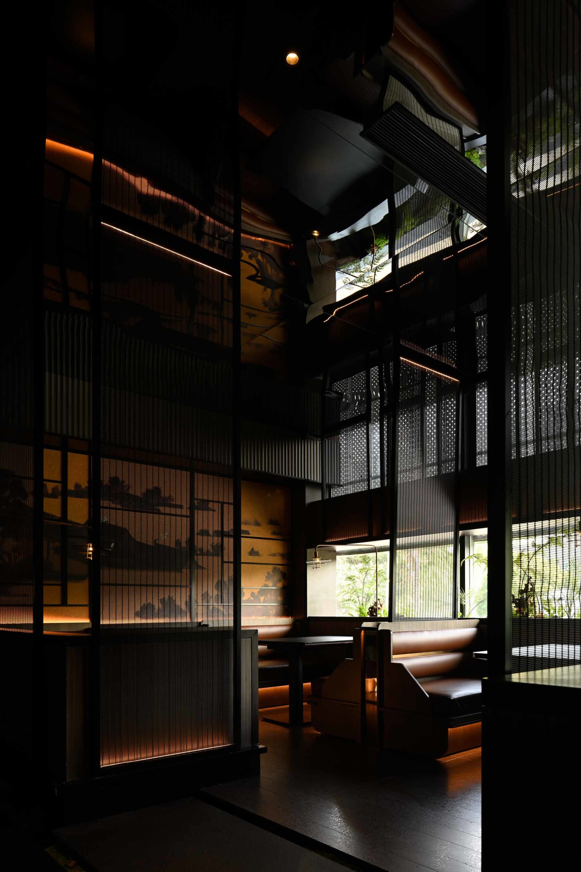 A modern industrial restaurant interior with dark walls, metal railings, and window lighting creating a warm atmosphere.