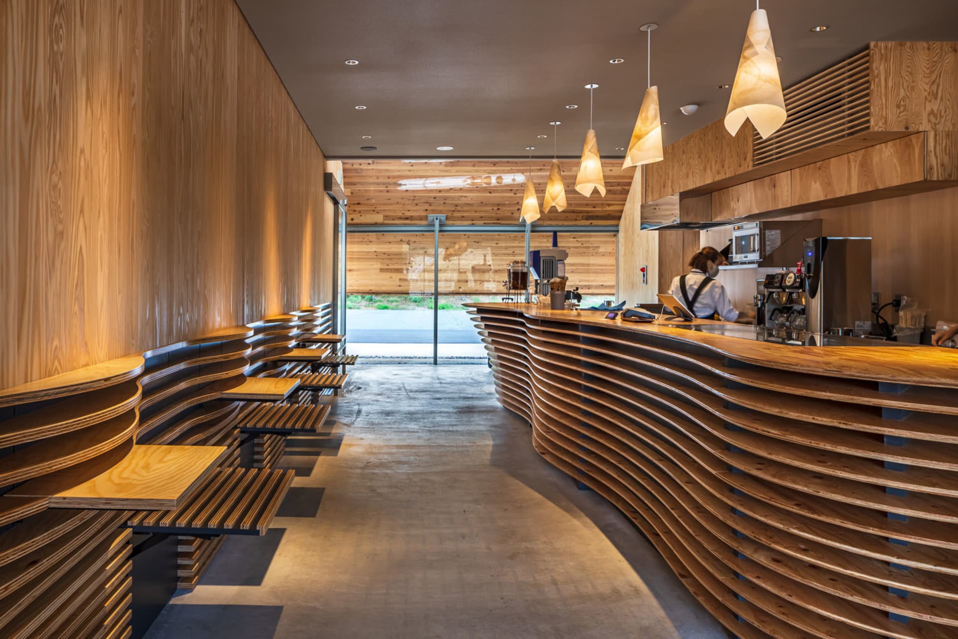 A modern coffee shop with a wooden interior featuring a counter and seating arrangements.