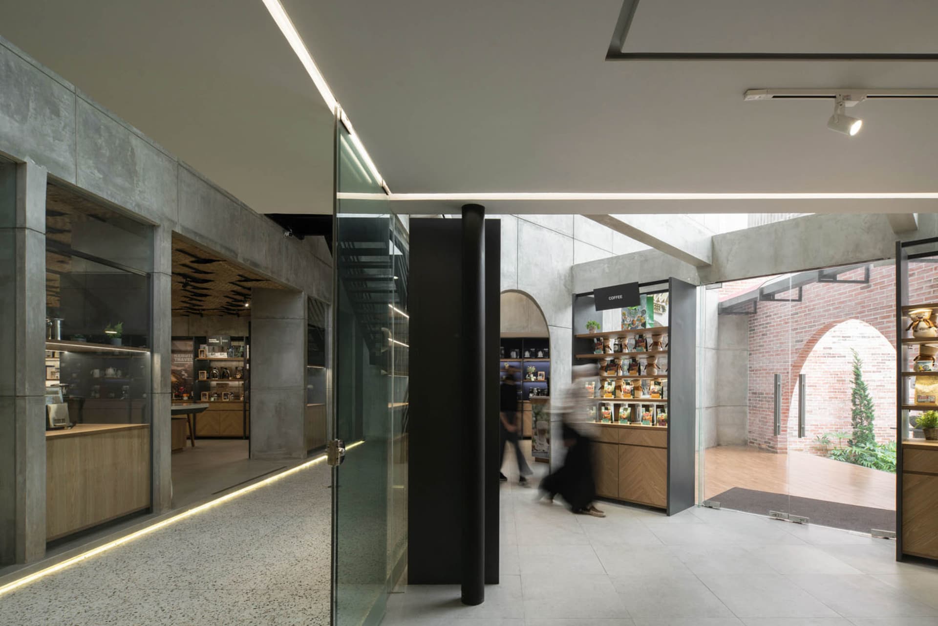 Minimalist coffee shop interior with concrete walls, glass shelves, and wood accents.
