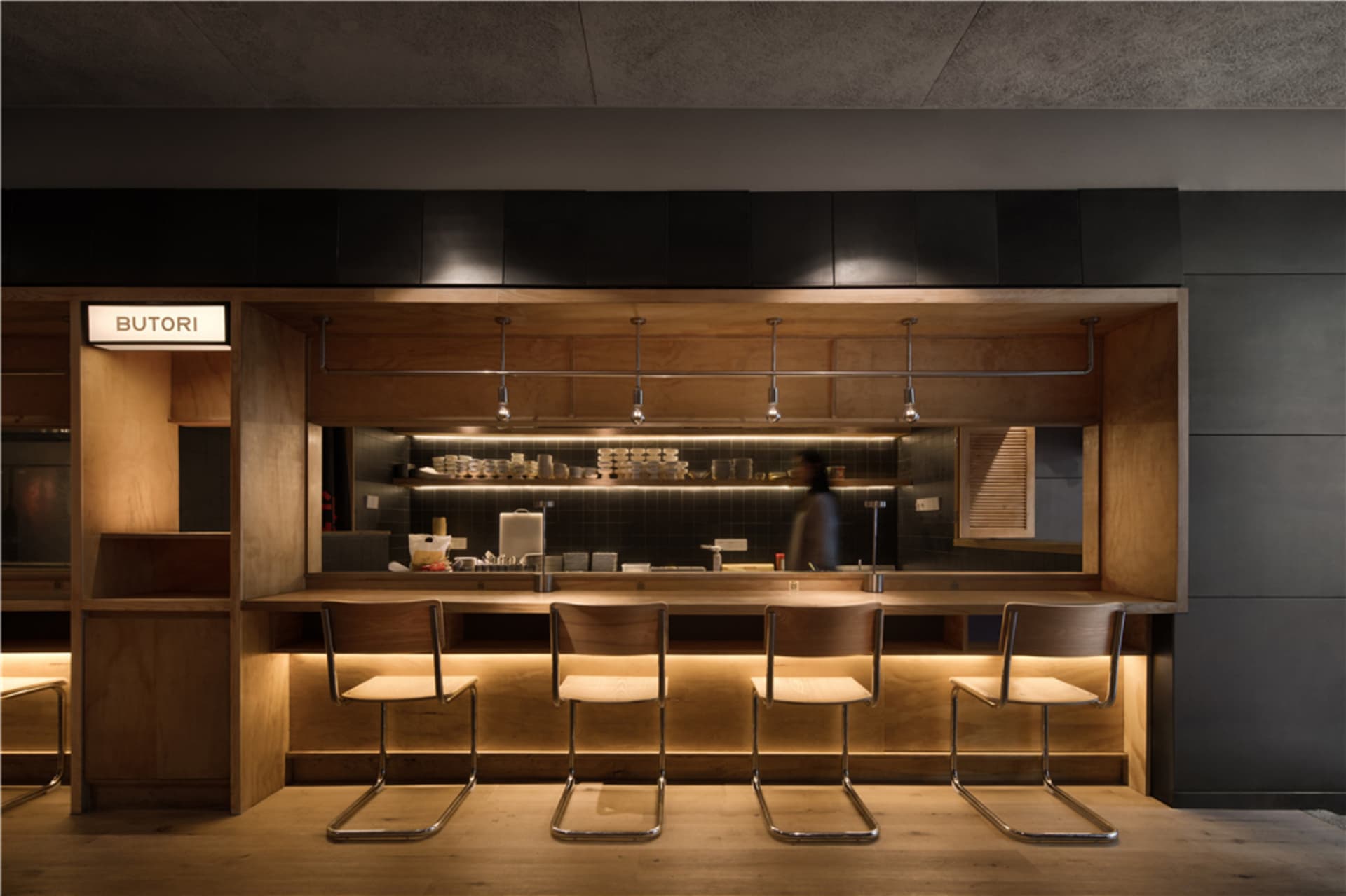 A modern, industrial-style restaurant counter with wooden seating and stainless steel accents.