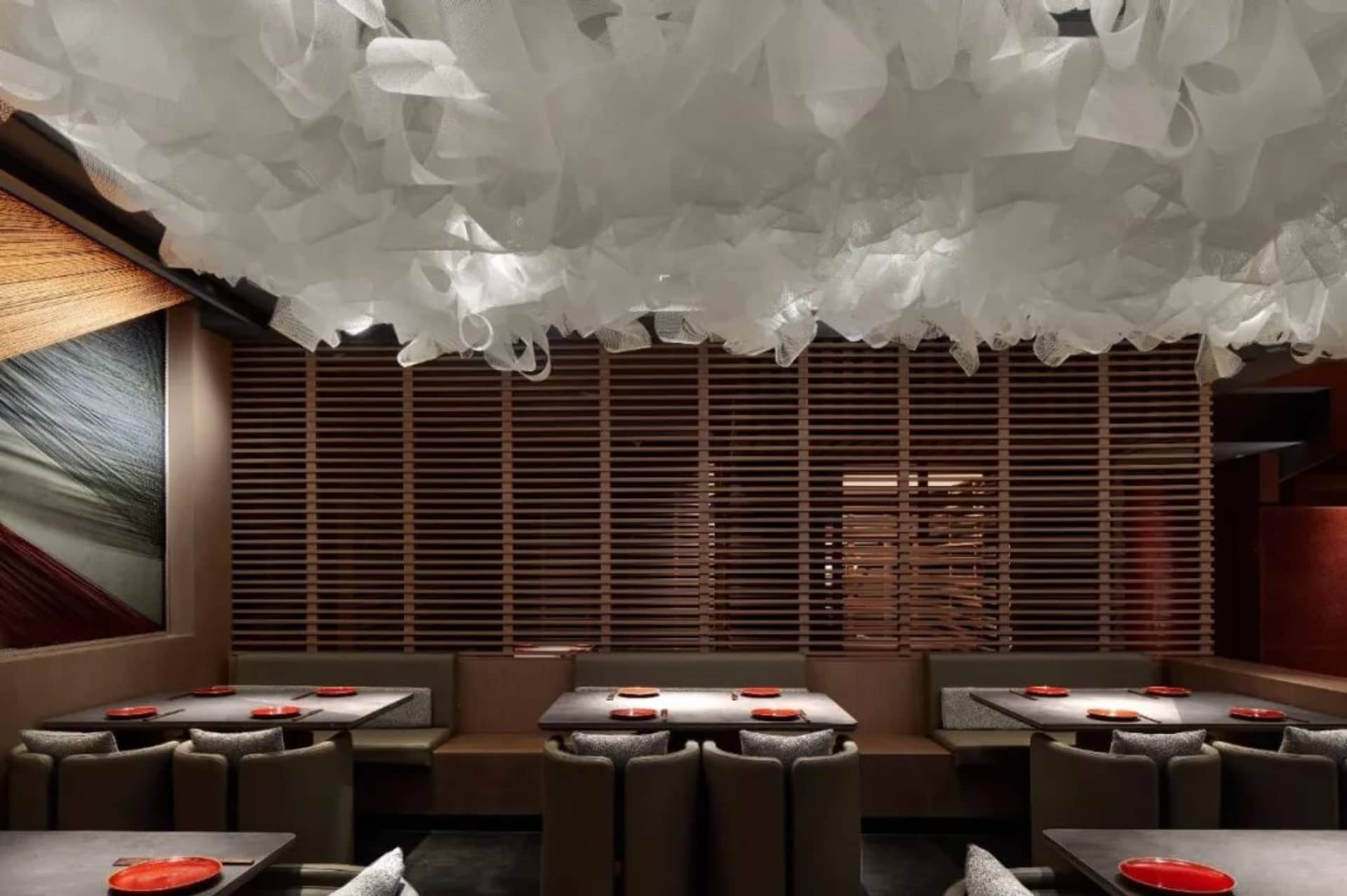 A modern restaurant interior featuring a white fabric ceiling, wooden slatted walls, and sleek seating.