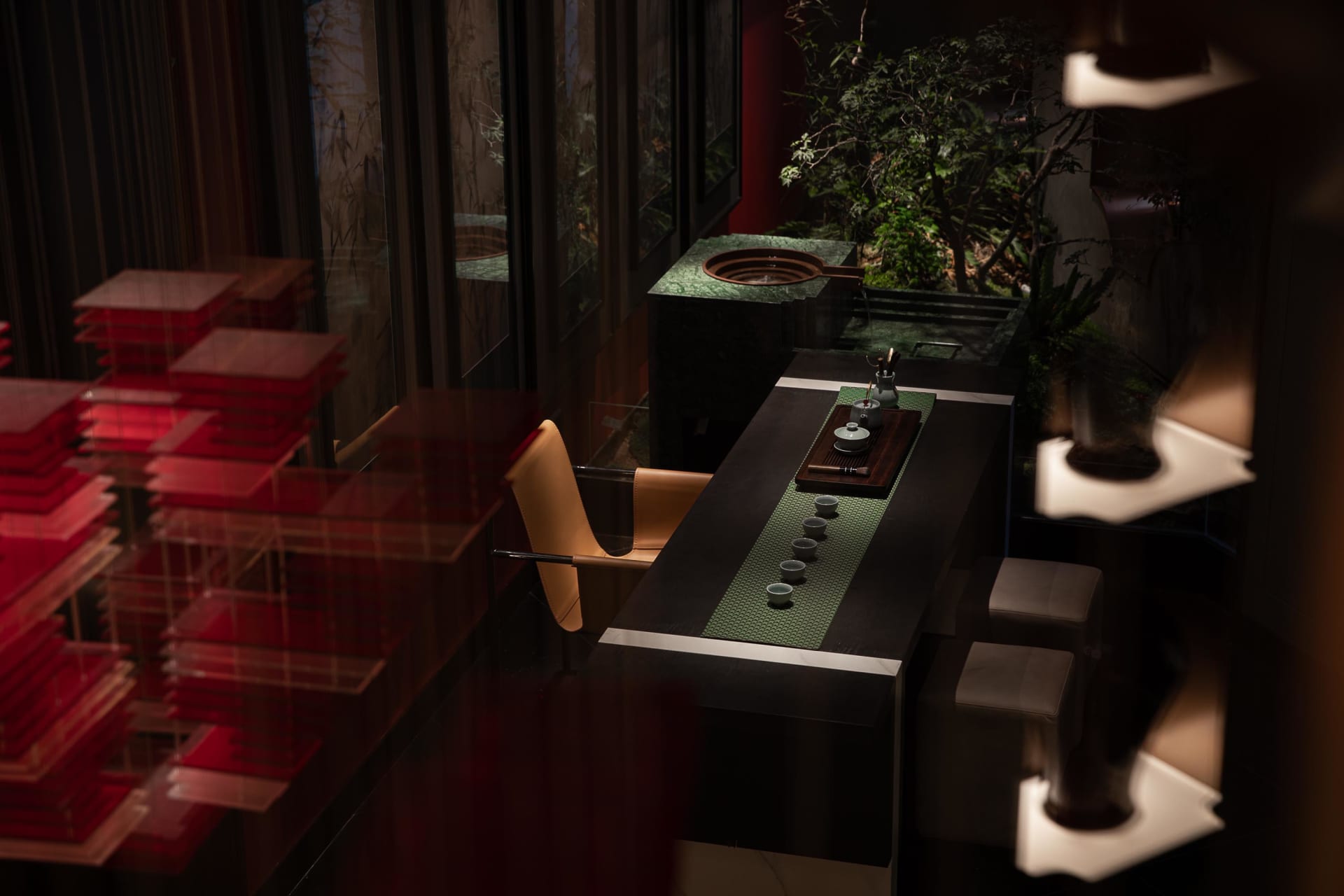 A modern industrial style tea ceremony space featuring dark wood, leather, green textiles, and glass elements.