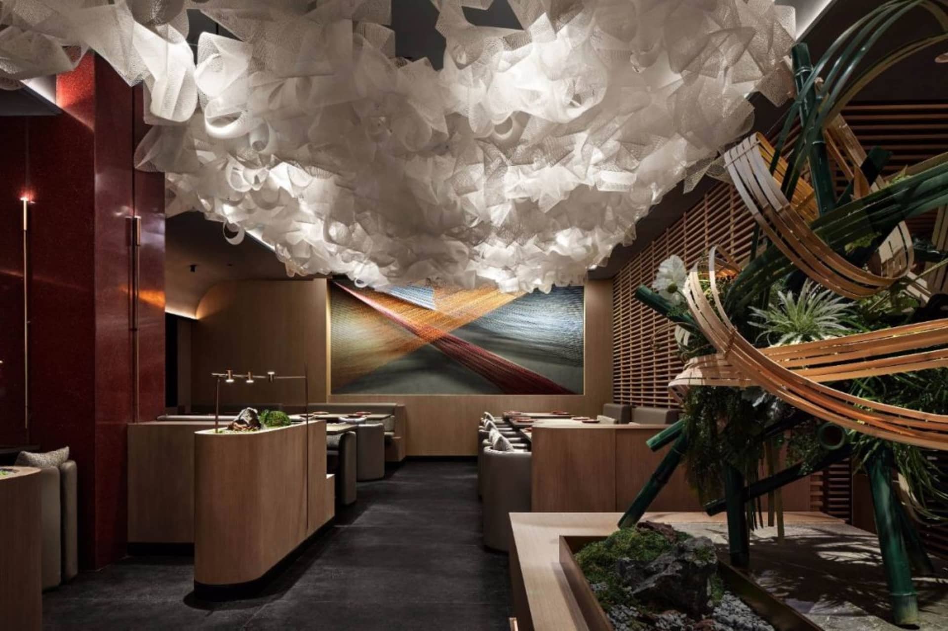 Modern restaurant interior with a white organic cloud ceiling, bamboo structure, and a waterfall fountain centered on a red a