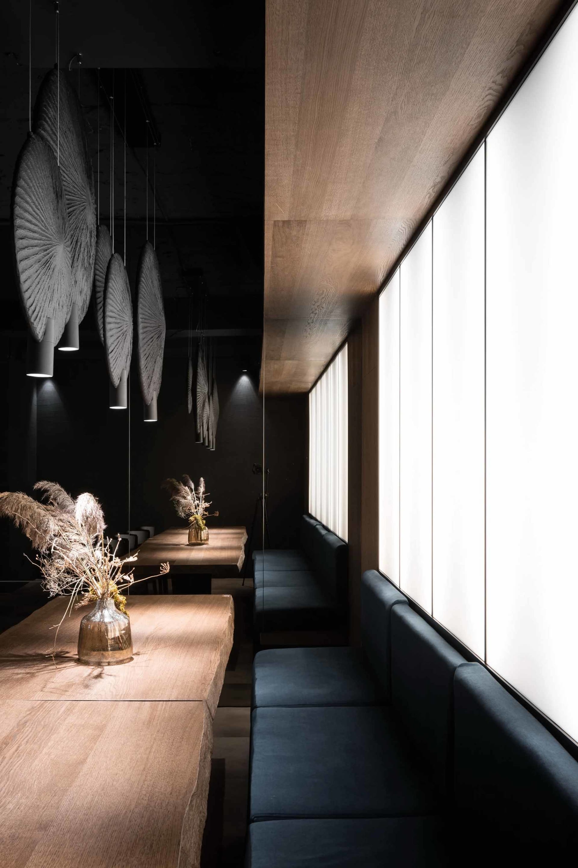 Modern minimalist restaurant interior with wooden tables, leather benches, and geometric ceiling lights.