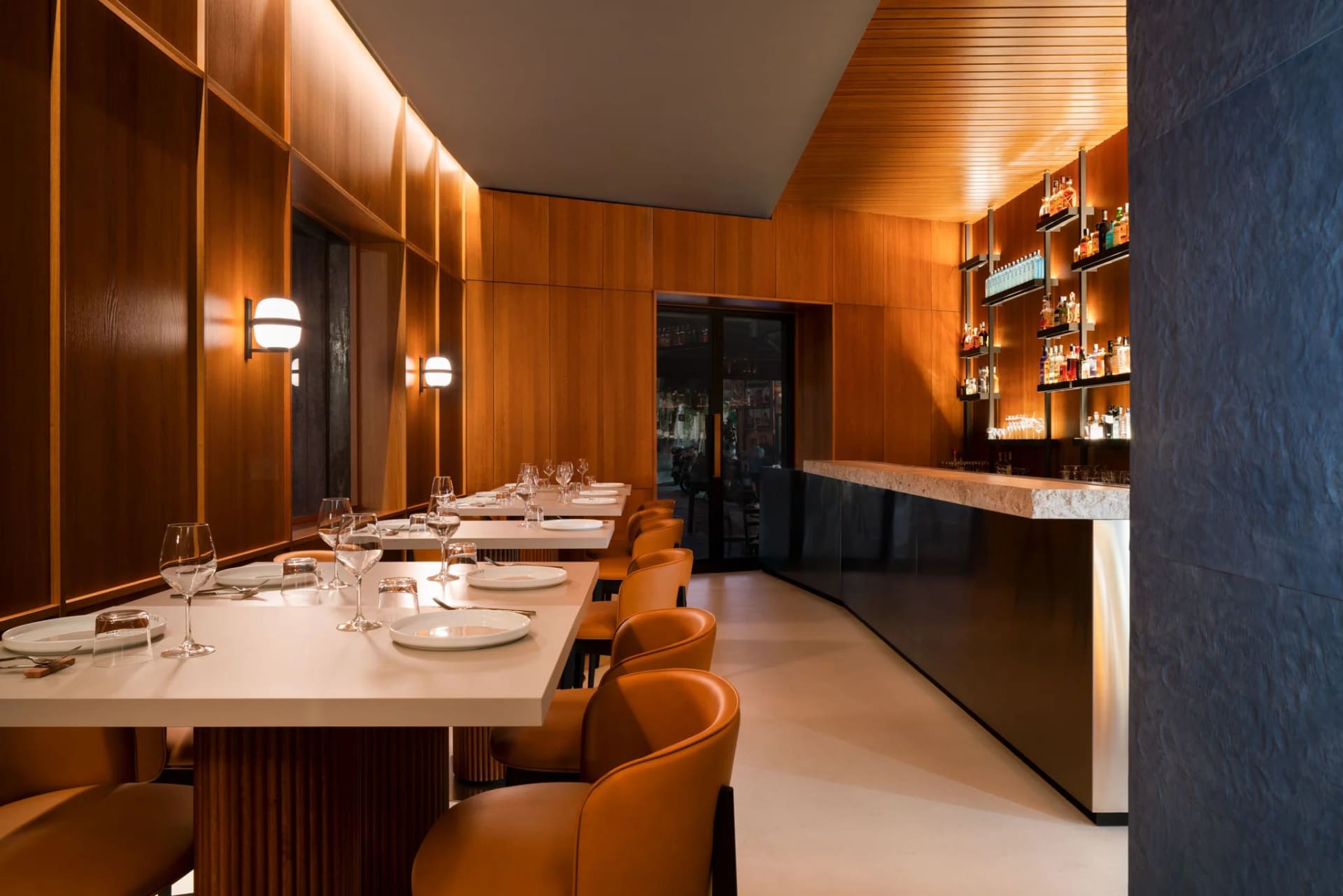 Modern restaurant interior with concrete and leather materials, featuring tables, chairs, and a bar counter.