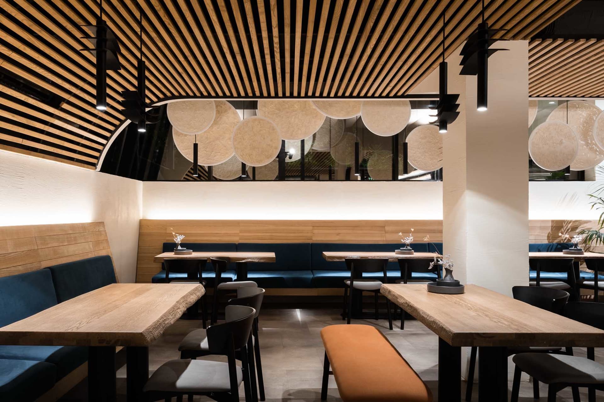 Modern restaurant interior with wooden tables and chairs, featuring a contemporary design with a mix of wood and metal materi