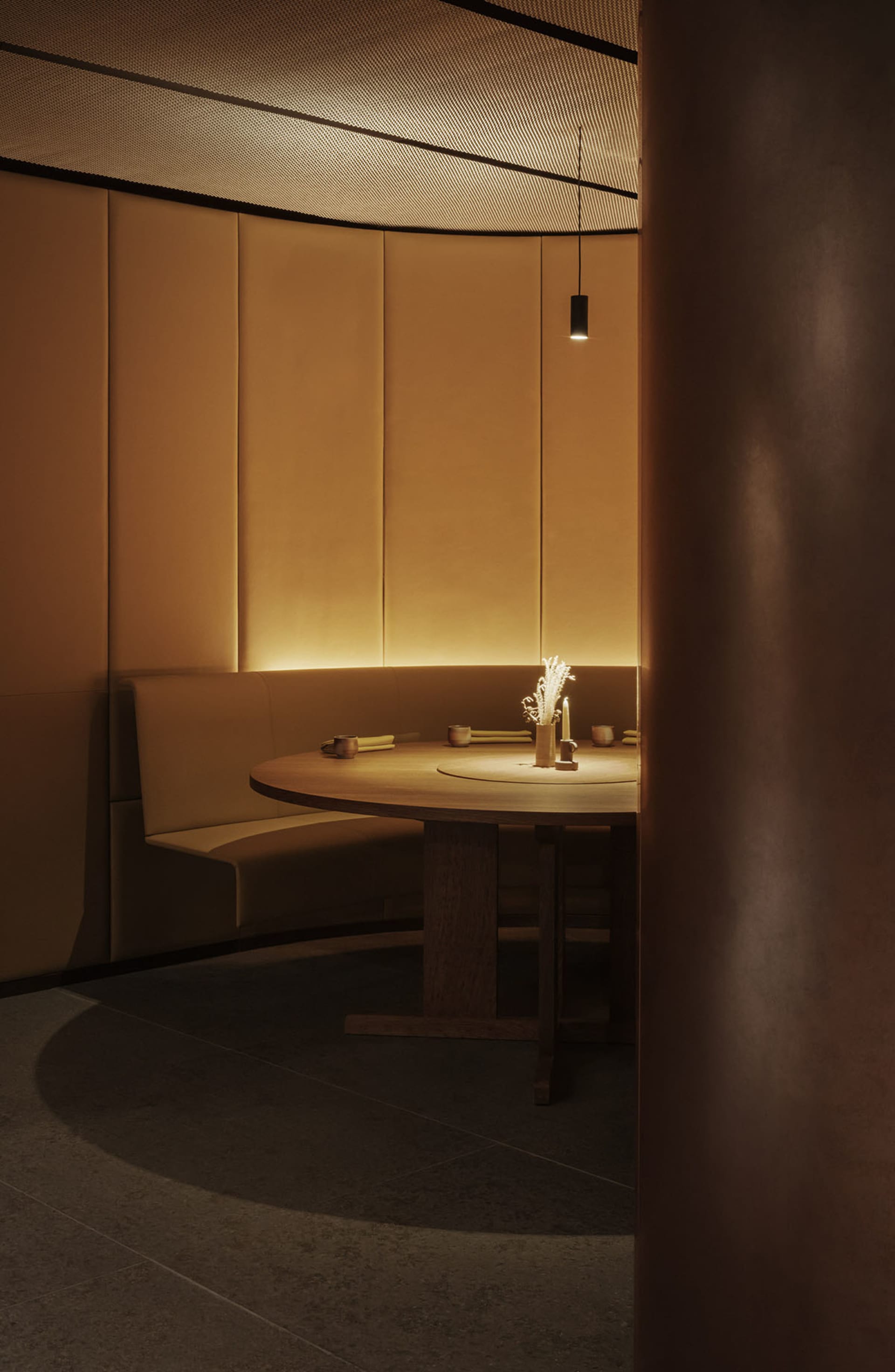 A minimalist restaurant dining room with a round wooden table, leather seating, and warm lighting.