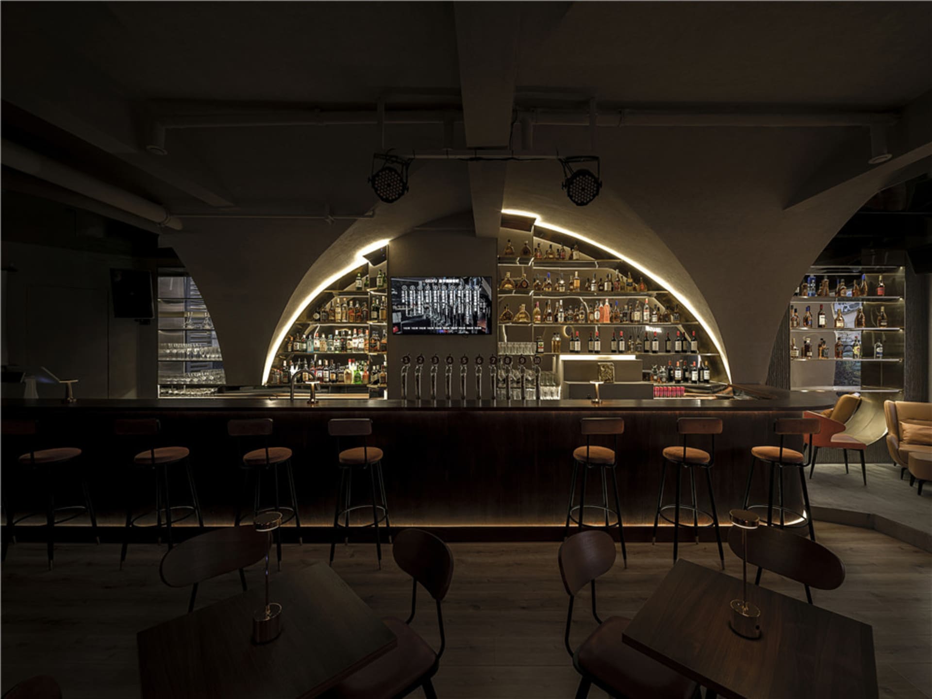 A dimly lit bar with arched ceilings, wooden furniture, and a variety of drinks on shelves.
